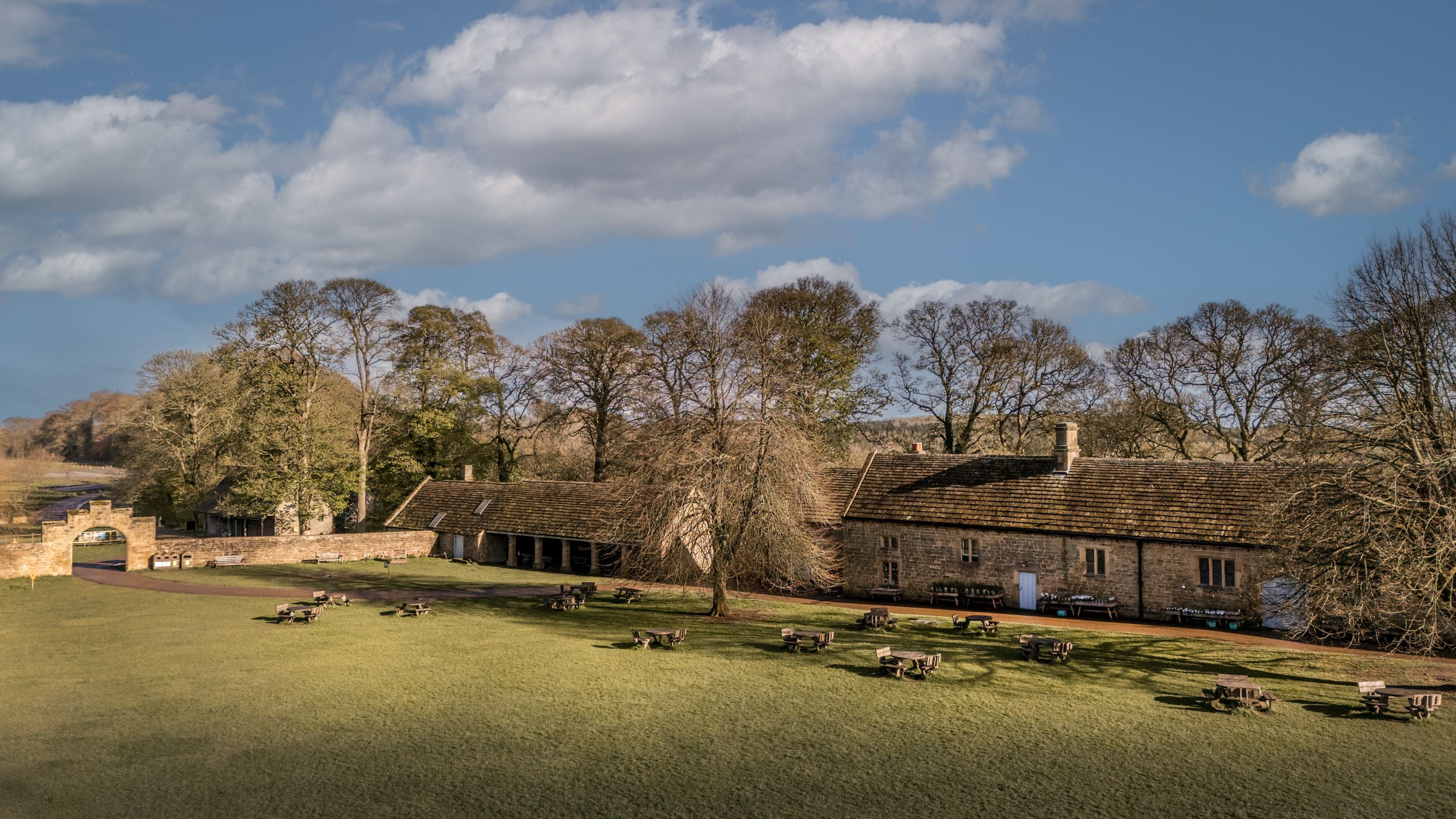 The old stone stables and grassy field that make up Hardwick's Stable Yard, next to the holiday cottages 6 High Hazels and 4 Stable Yard Cottage, Derbyshire