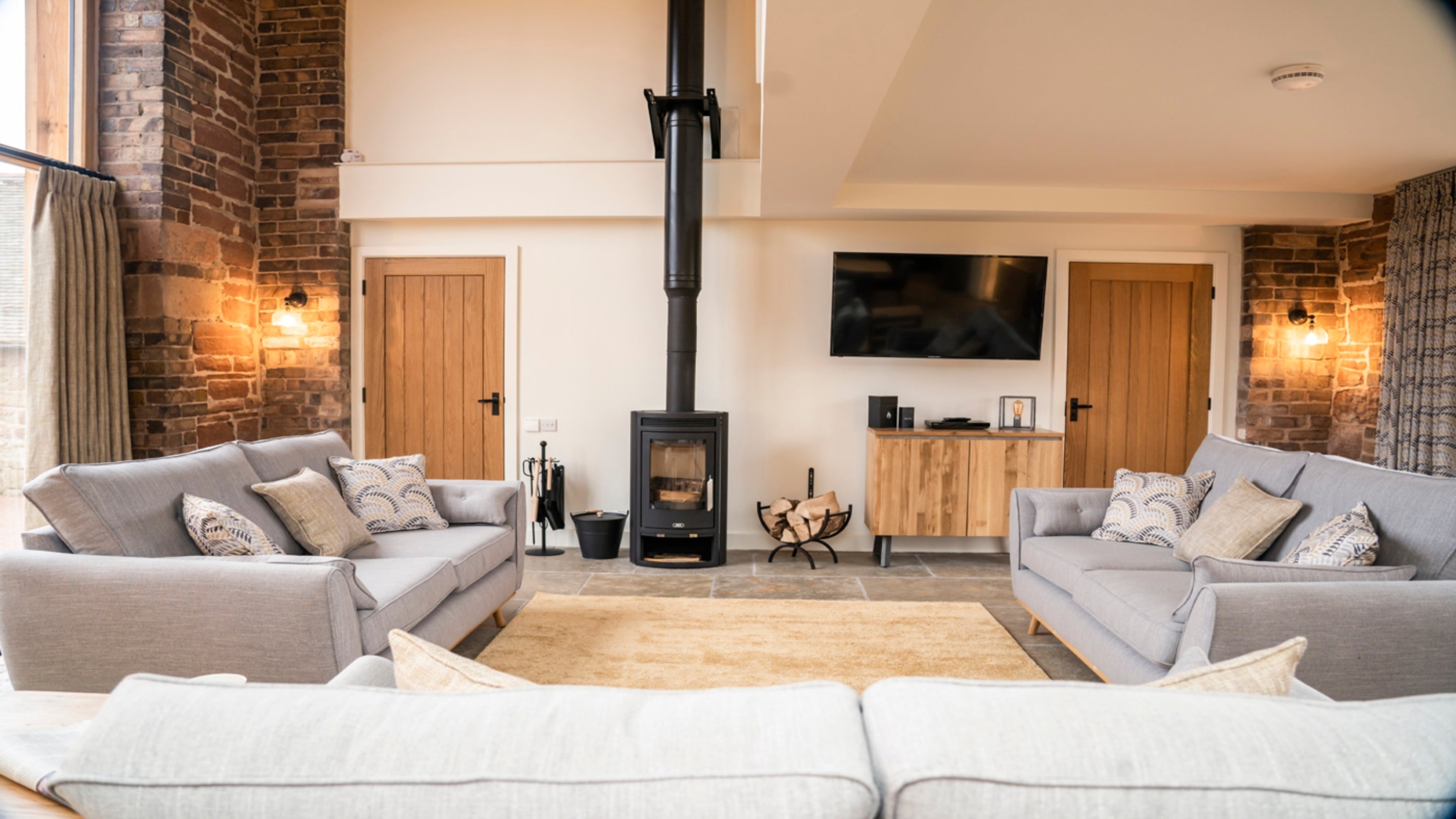 The sitting area in the open-plan living space of Sandybury Barn, with three sofas, television, woodburner and a vaulted ceiling, Shropshire
