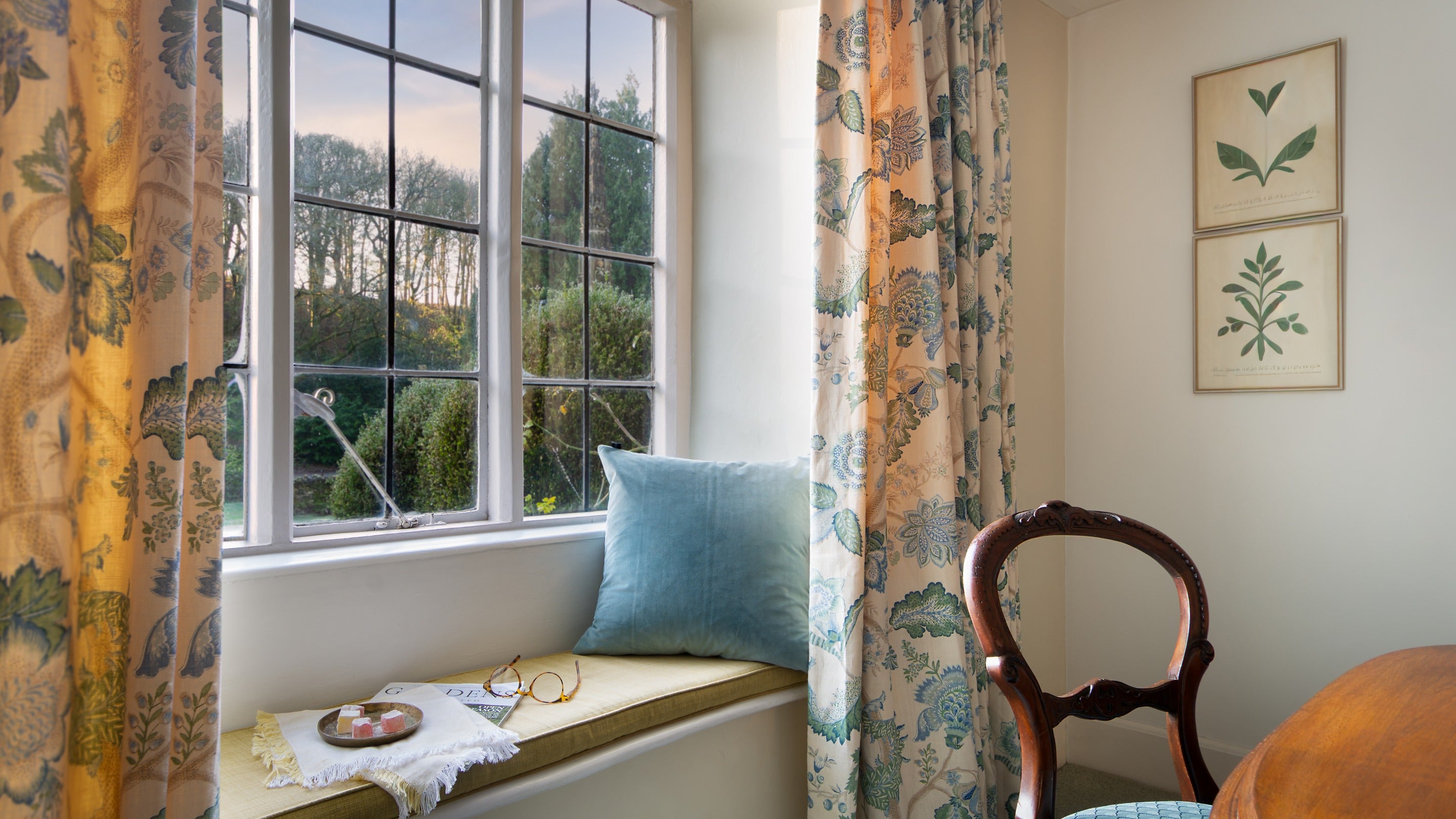 The cushioned window seat in the dining room at 89 Church Lawn, with views over the front garden and the medieval church beyond, Wiltshire