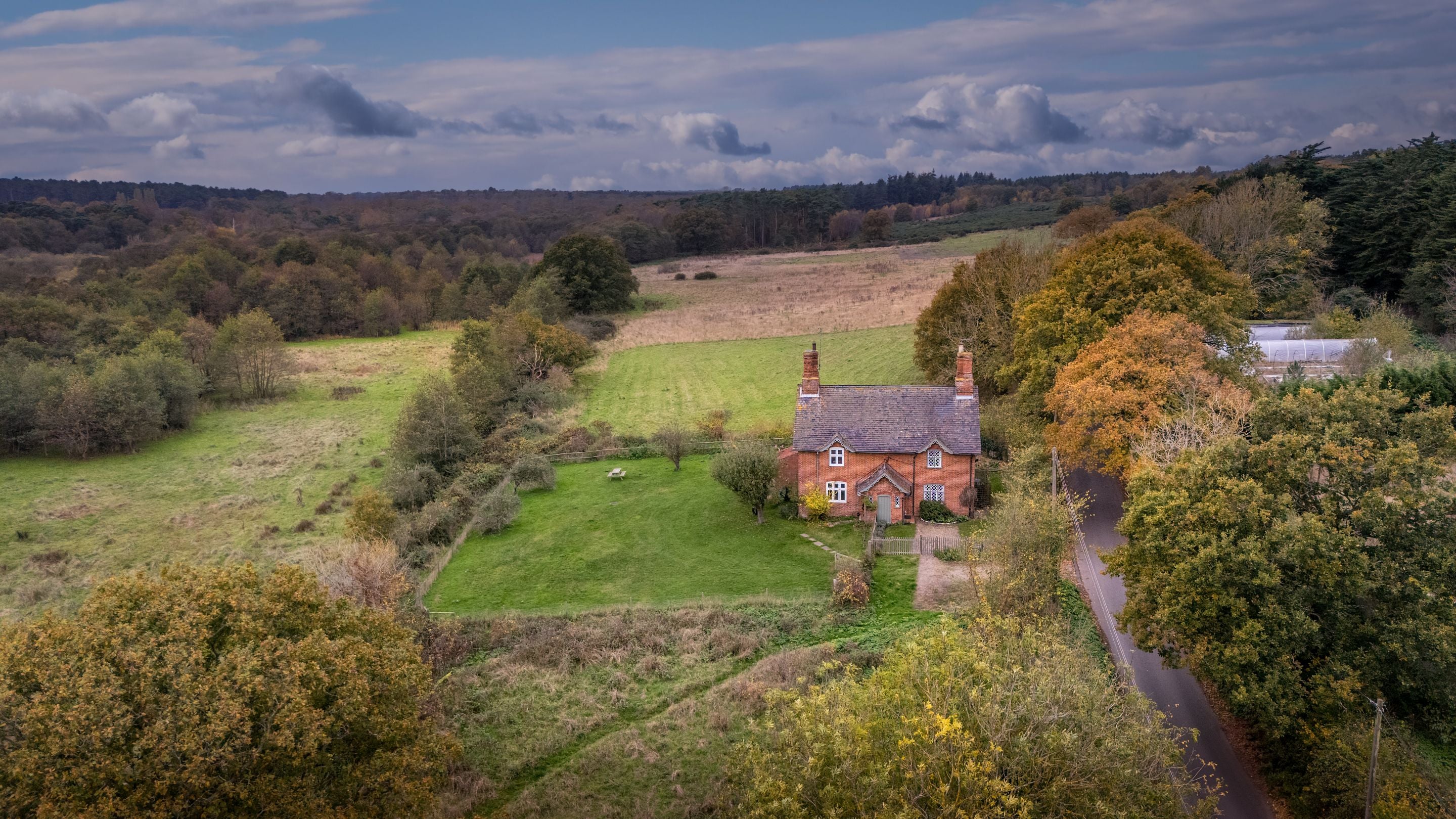 An aerial view of Bridge Farm Cottage on the right and the adjoining cottage on the left, surrounded by fields and woodland, Suffolk