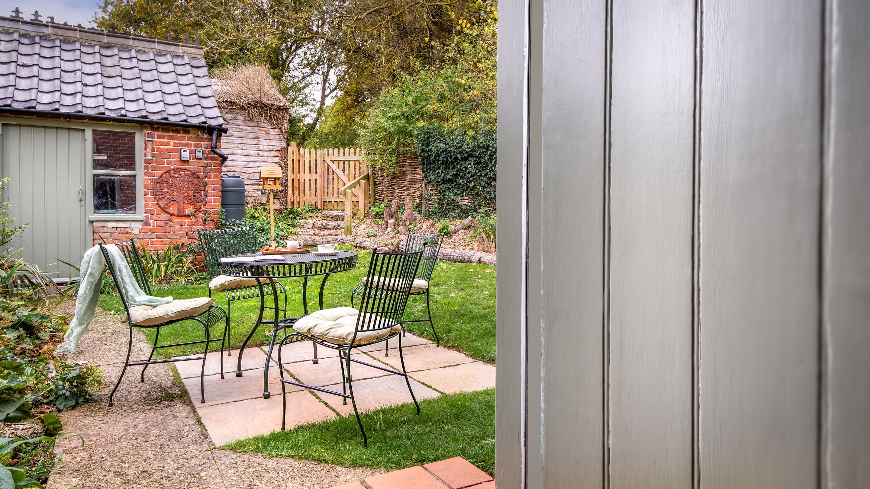 Looking into the back garden of Bridge Farm Cottage at the small patio with outdoor dining furniture, the lawn and the shed, Suffolk