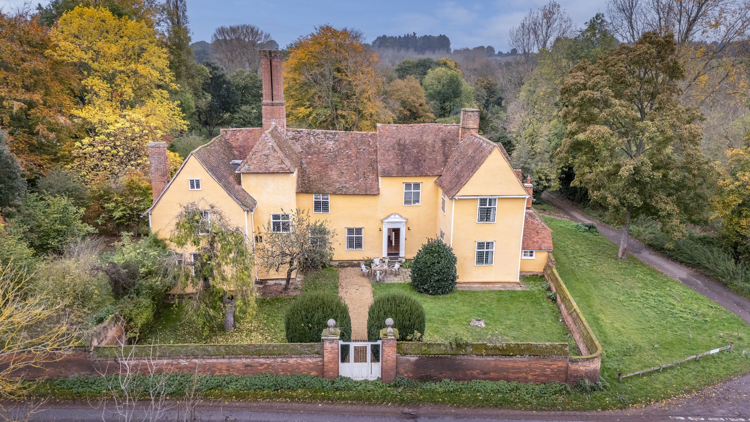 An aerial view of Thorington Hall and its walled southern garden, with patio, outdoor dining furniture, lawn and trees, Suffolk