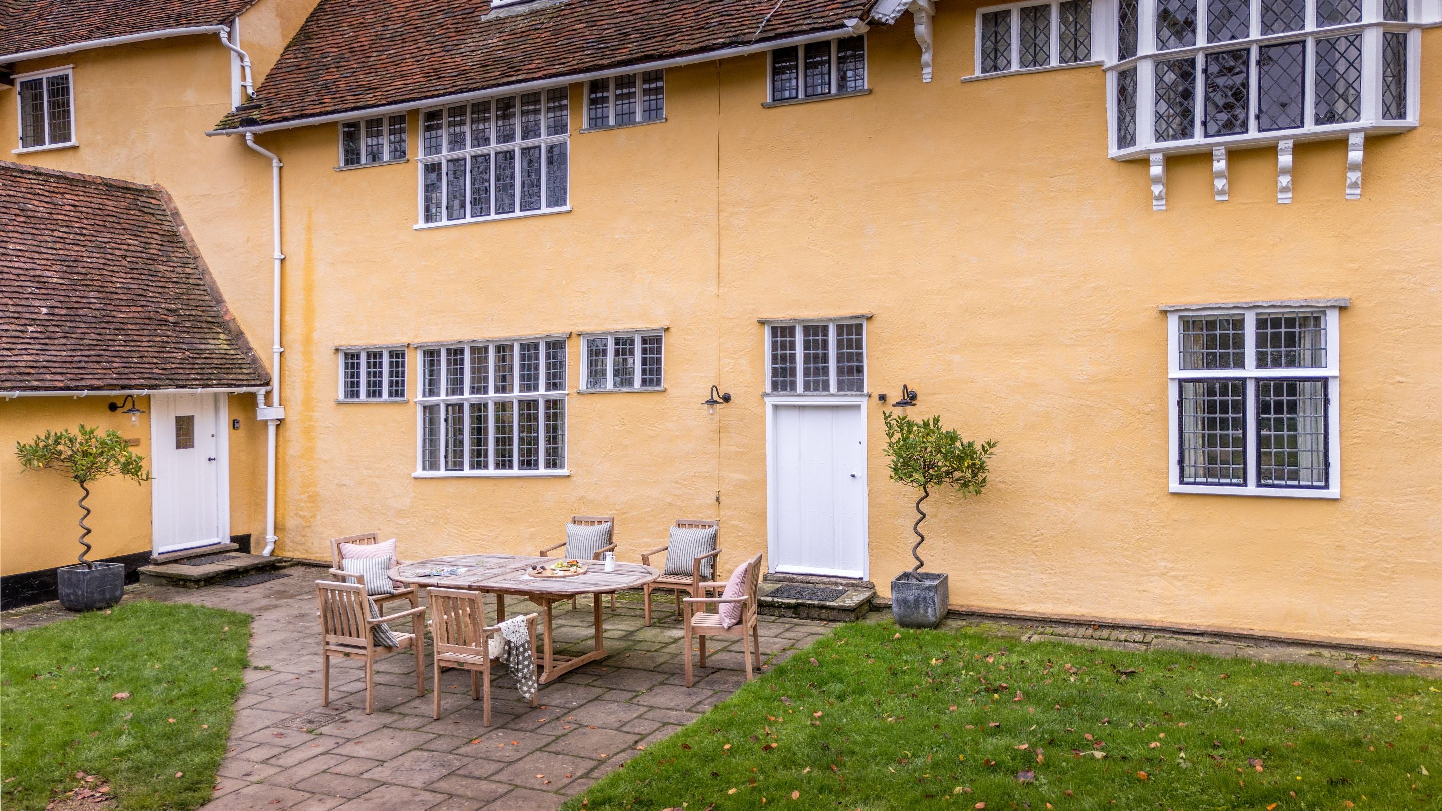 The northern terrace with patio and outdoor dining furniture and the main entrance to Thorington Hall on the left, Suffolk