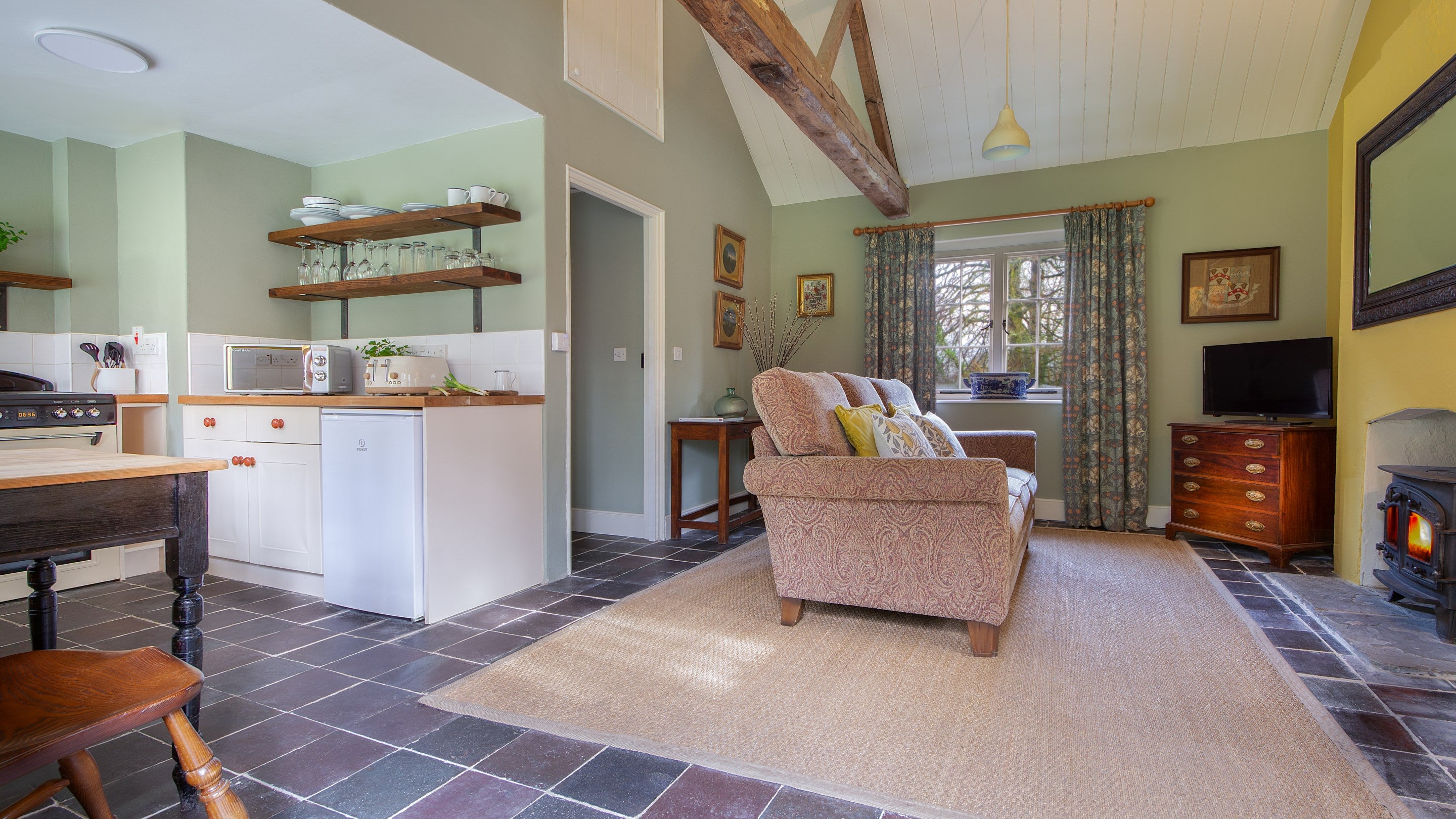 The open-plan living space at Cariad Cottage, with kitchen, table for two, sofa, television and woodburner, Carmarthenshire