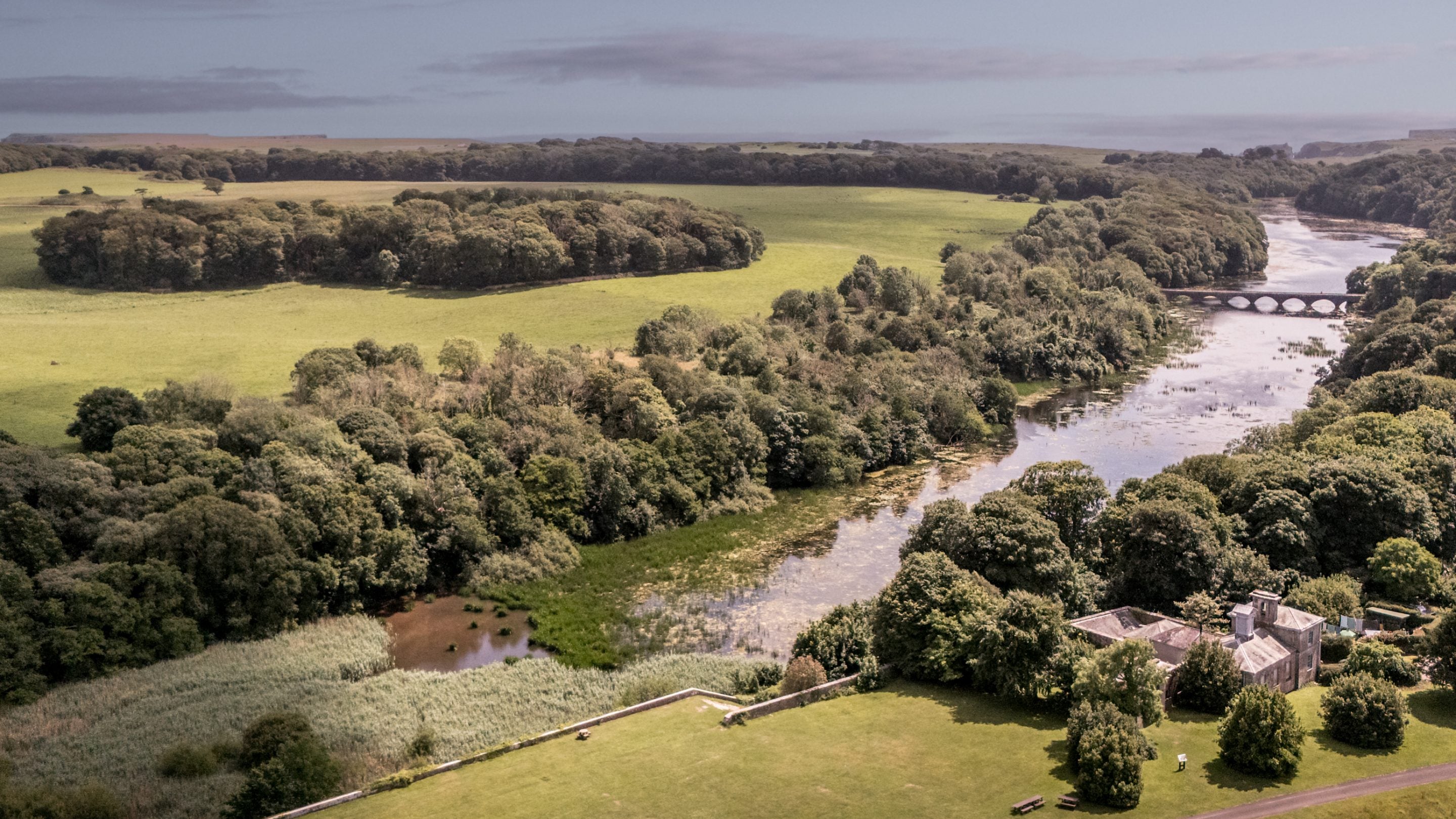 An aerial view of Cawdor and Stackpole's lakes and parkland beyond, leading to the sea, Pembrokeshire