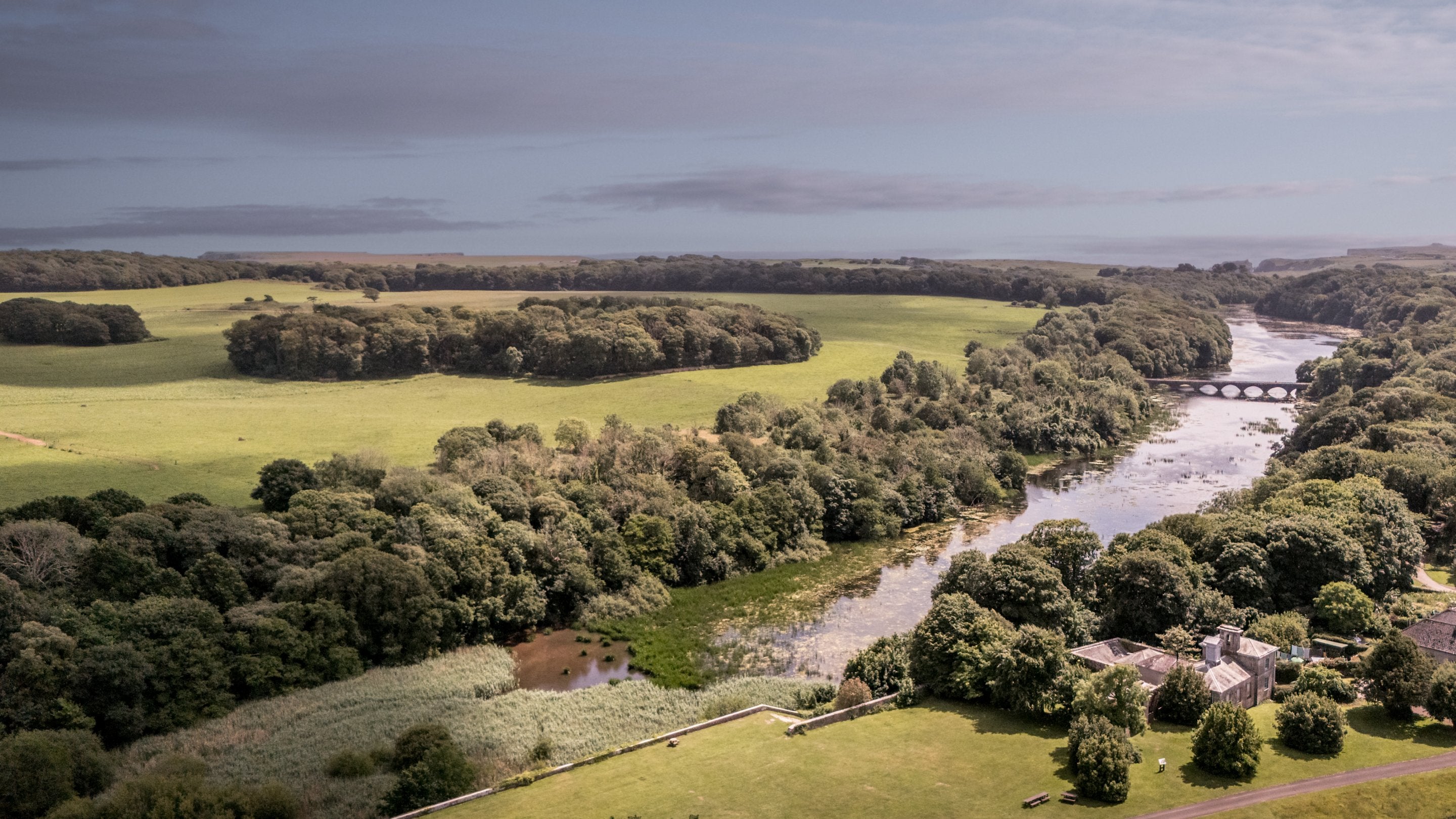 An aerial view of Cawdor and Stackpole's lakes and parkland beyond, leading to the sea, Pembrokeshire