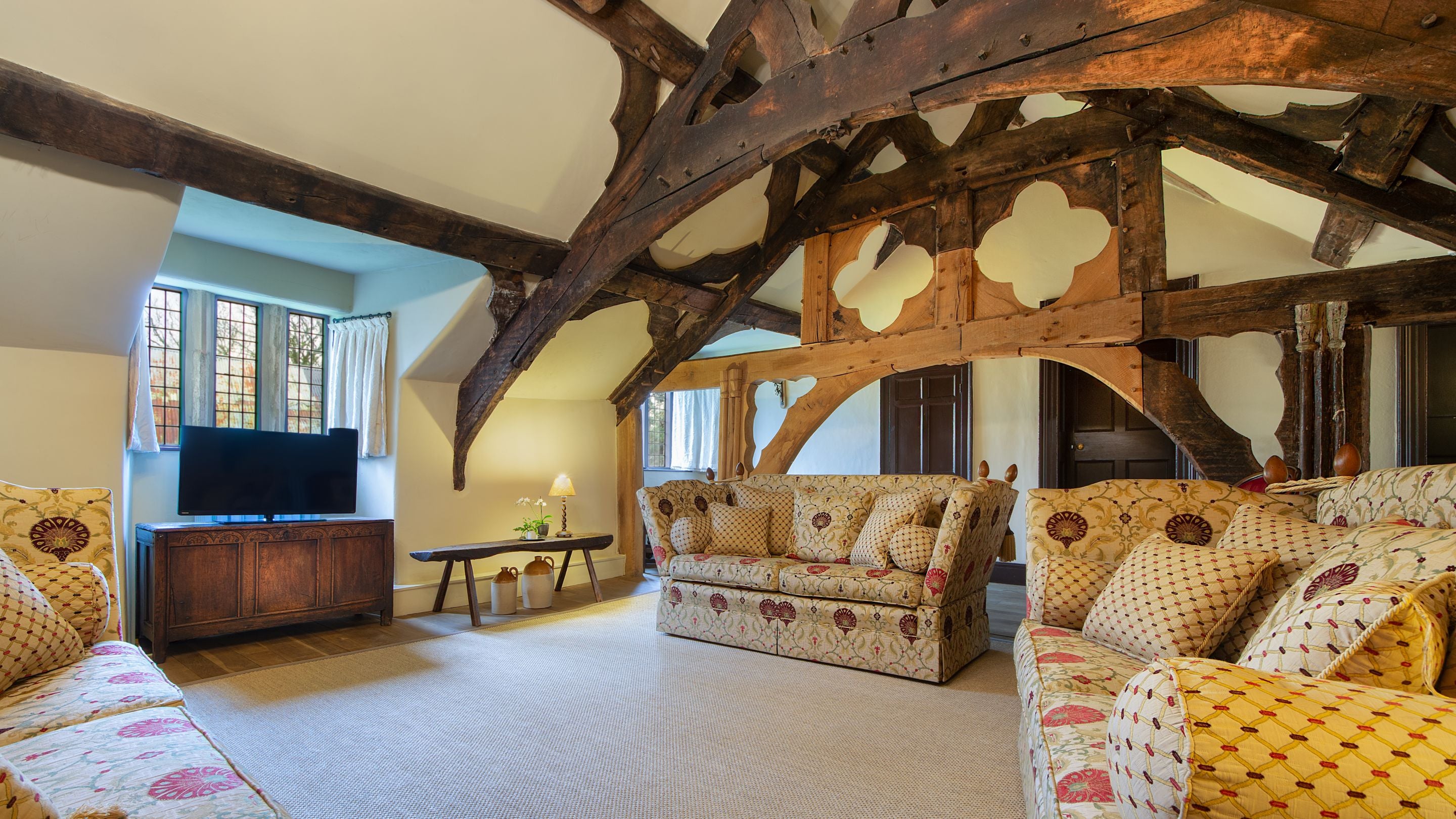 The medieval hall sitting room on the first floor of Egryn. The room has a vaulted ceiling, wooden beams, three sofas, a television and a small dining table, Gwynedd