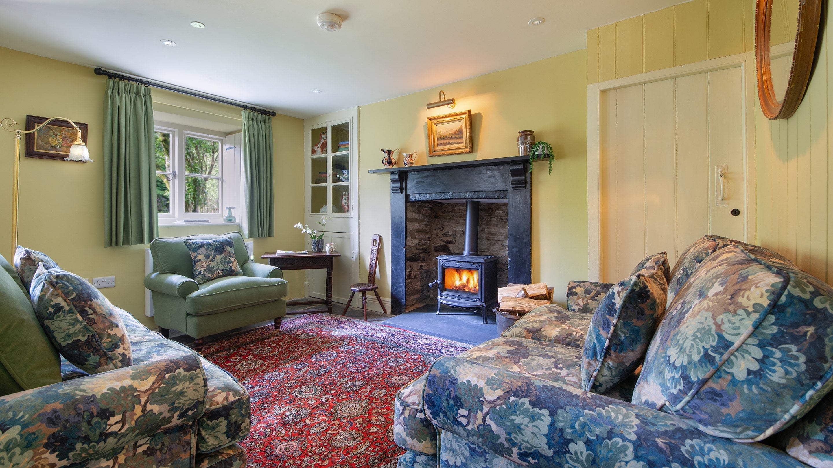 The sitting room at Hawthorn Cottage, with woodburner in the original inglenook, sofas and armchair, television and rug covering the original slate floor, Ceredigion