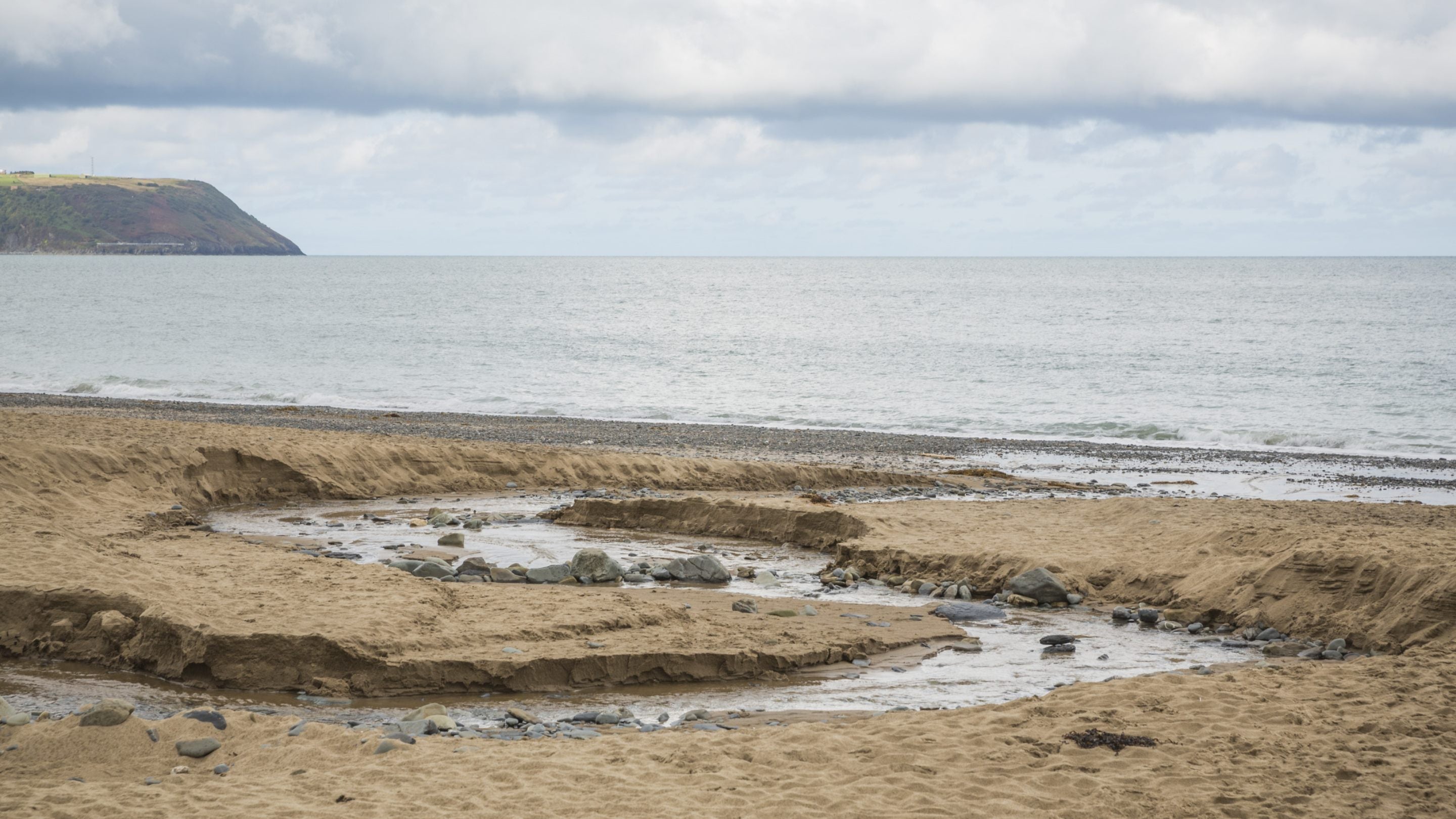 A stream carves its way through the sand towards the sea at Penbryn, Ceredigion, Wales
