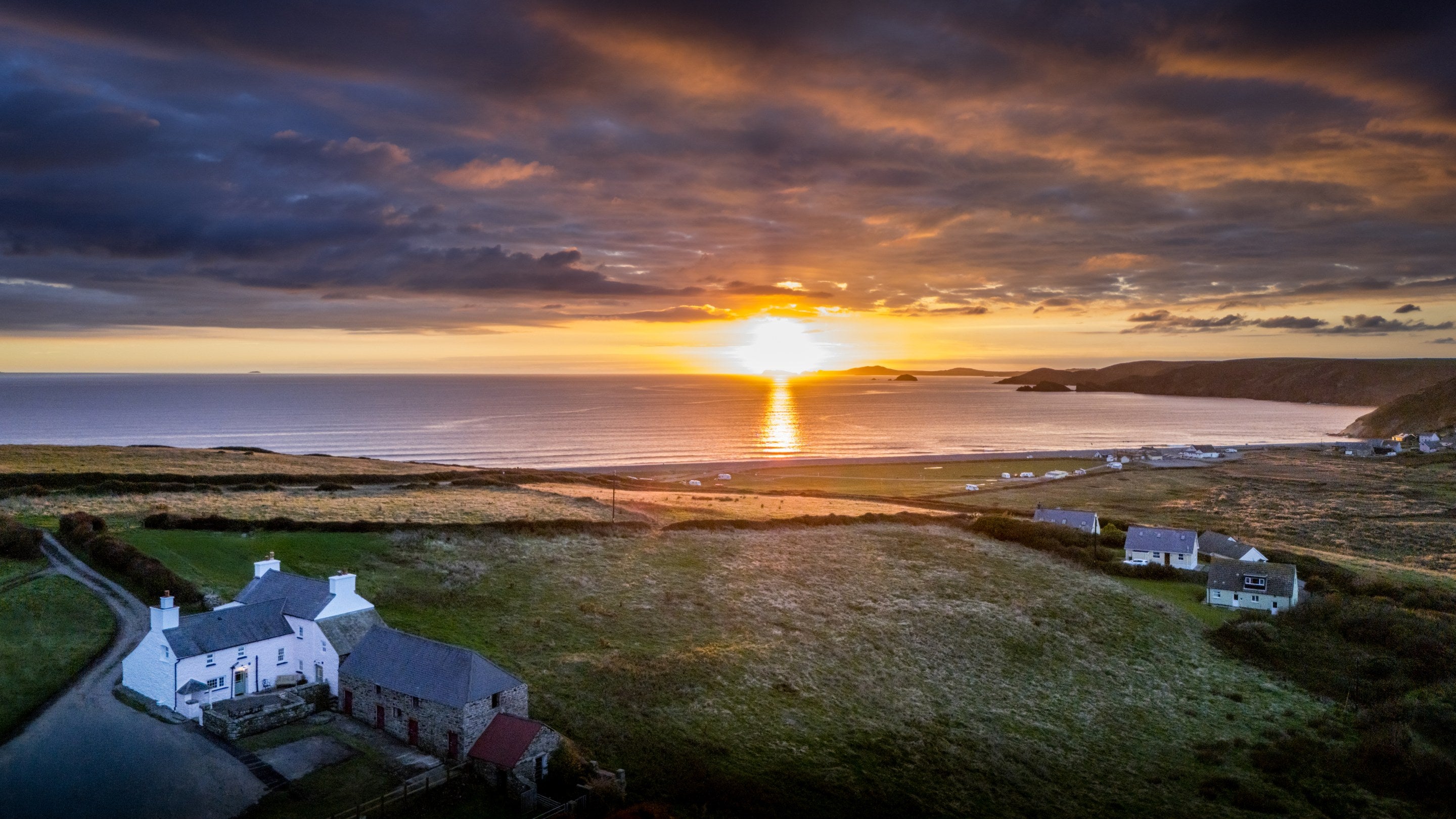 An aerial view of Newgale Wood Farm (on left) at sunset, with countryside and Newgale beach in the background, Pembrokeshire