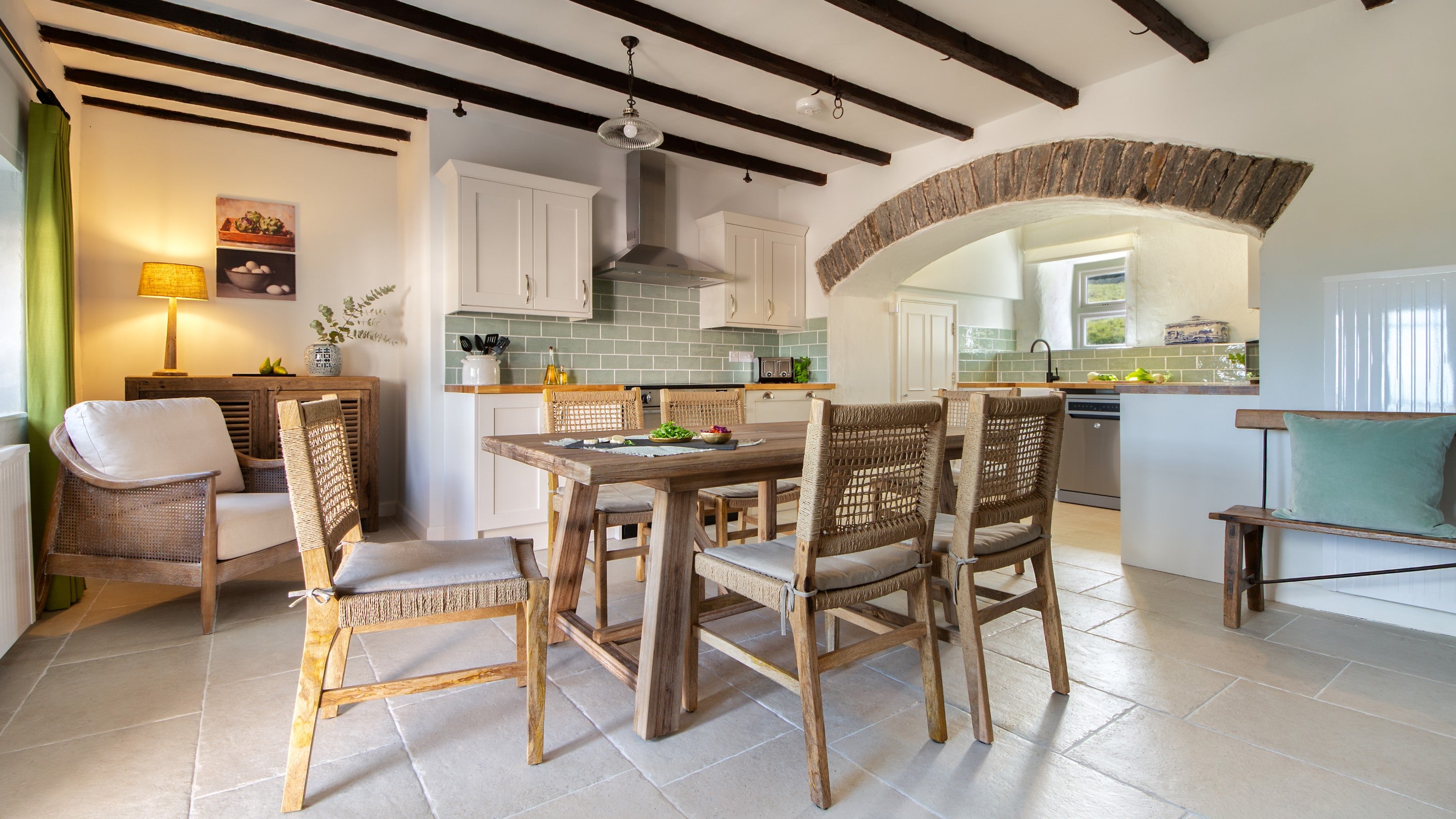The kitchen with dining table for six and original beams and stone ceiling arch, at Newgale Wood Farm, Pembrokeshire