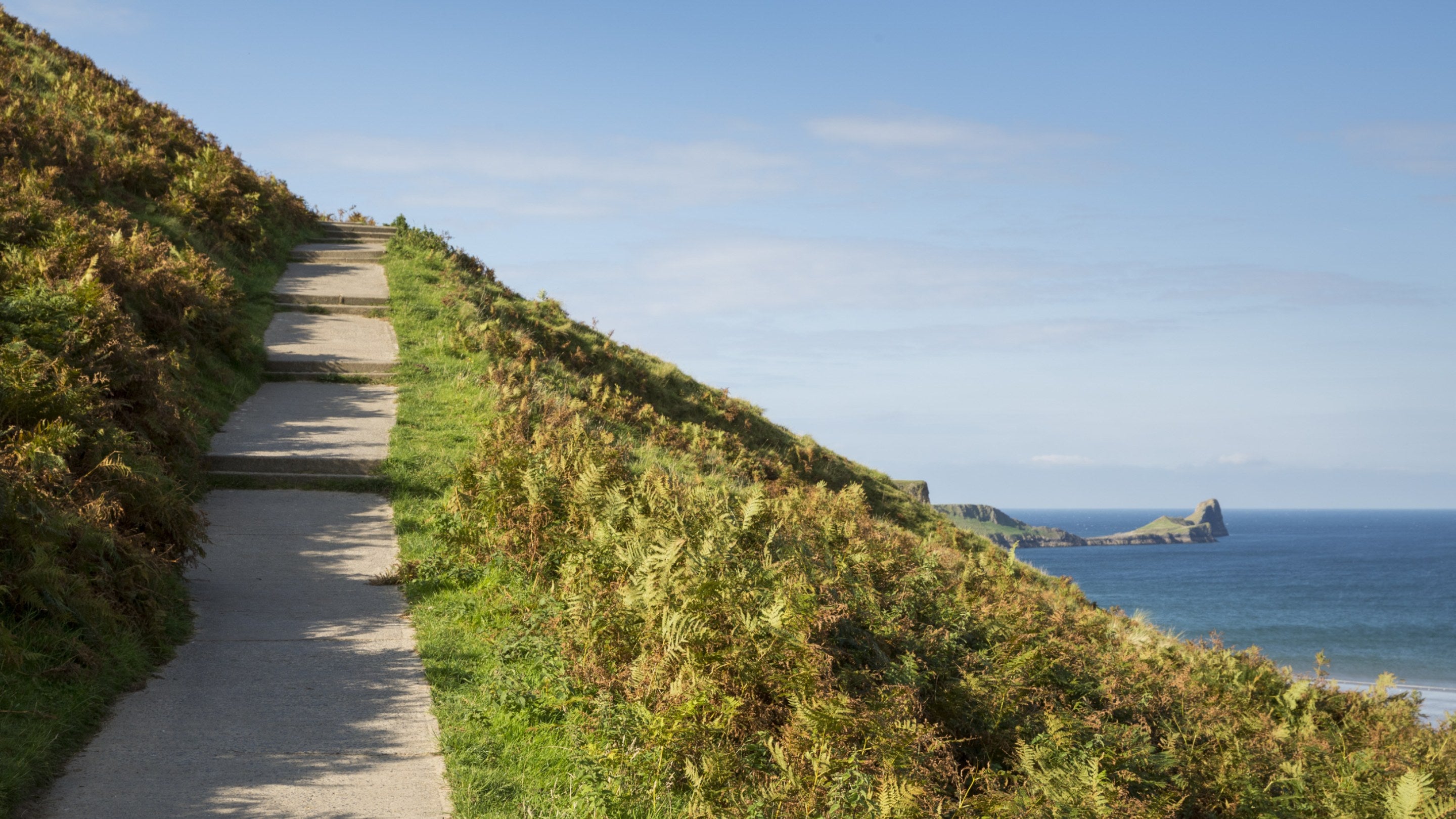 Coastal pathway climbing the cliffs at Rhossili Bay, with Worms Head Island in the distance, South Wales