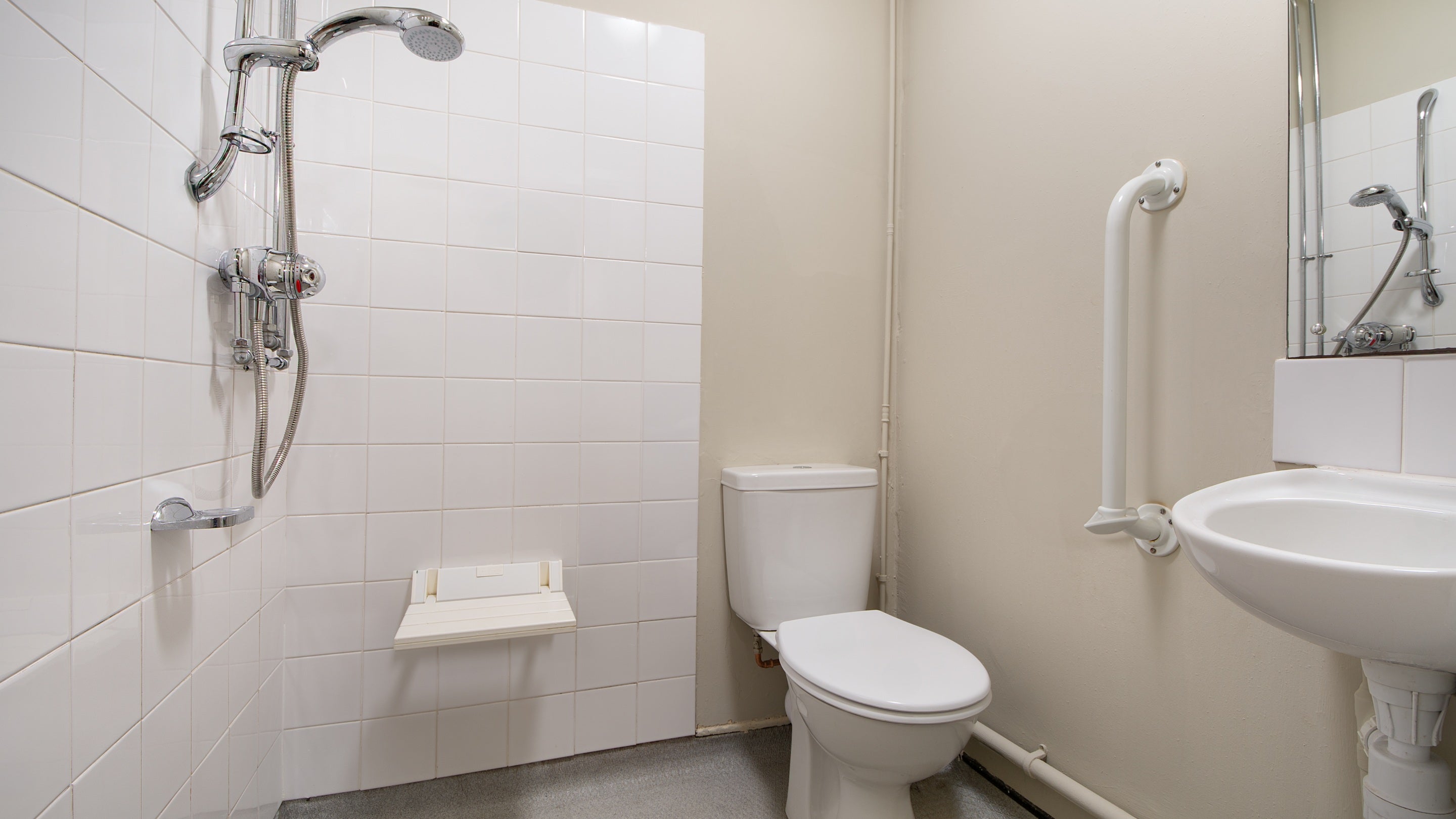 The accessible wet room with a toilet and sink, grab rails, and shower with seat, on the ground floor of Watkin Bunkhouse, Gwynedd