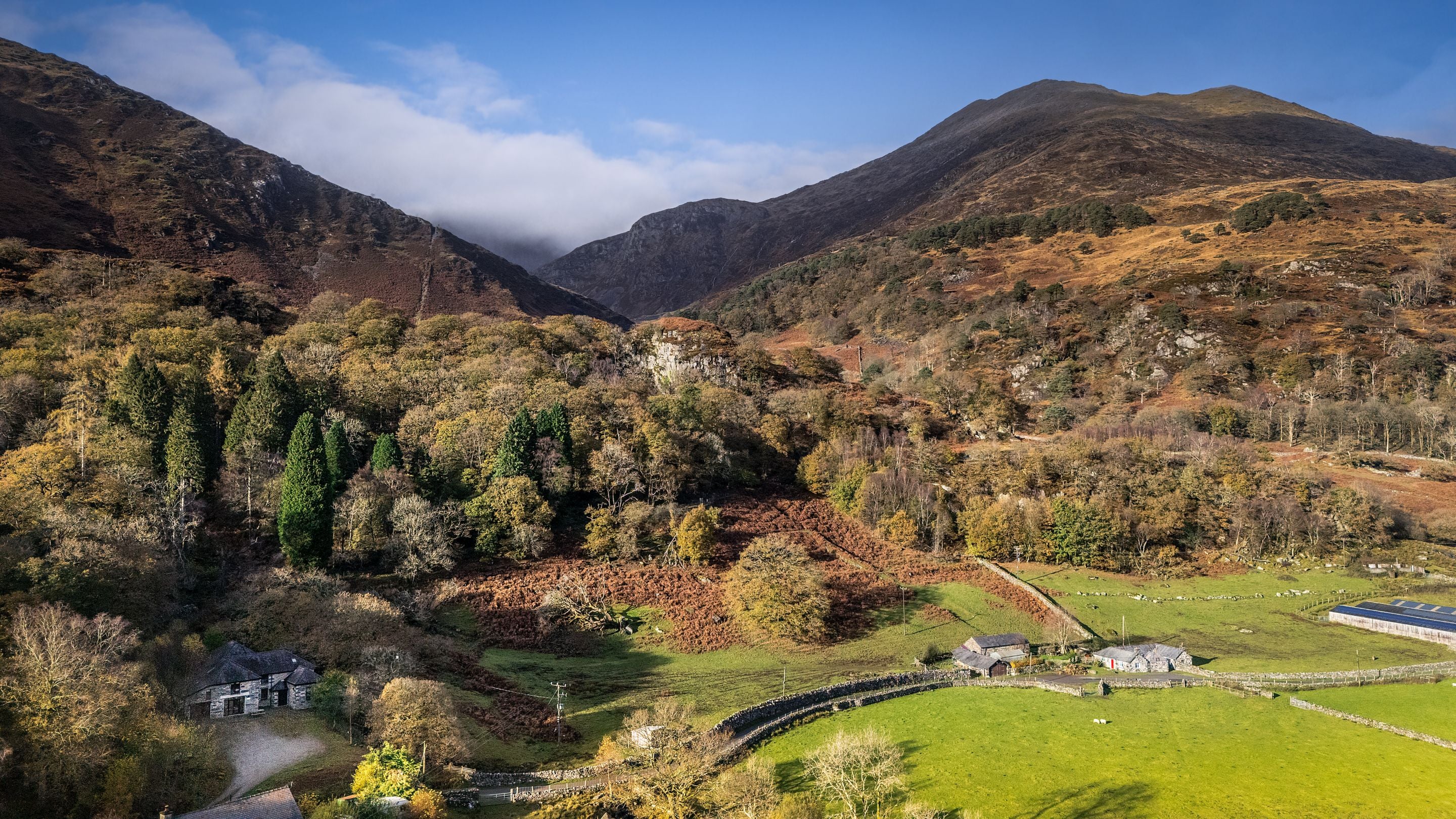 An aerial view of the Yr Wyddfa (Snowdon) range, with Watkin Bunkhouse in the bottom left corner and Yr Wyddfa covered by clouds in the distance, Gwynedd
