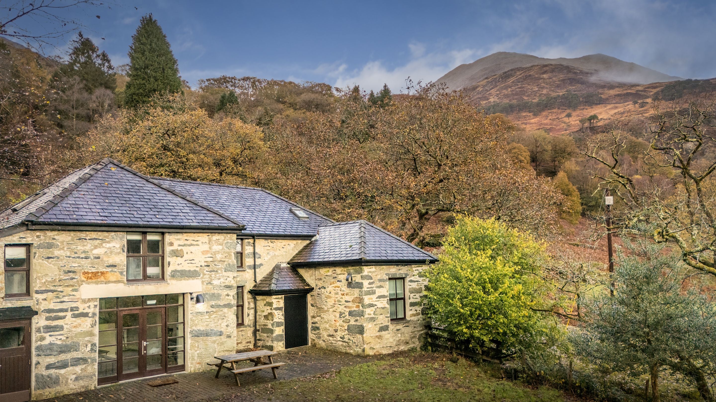 The front of Watkin Bunkhouse, with woodland and mountains in the background, Gwynedd