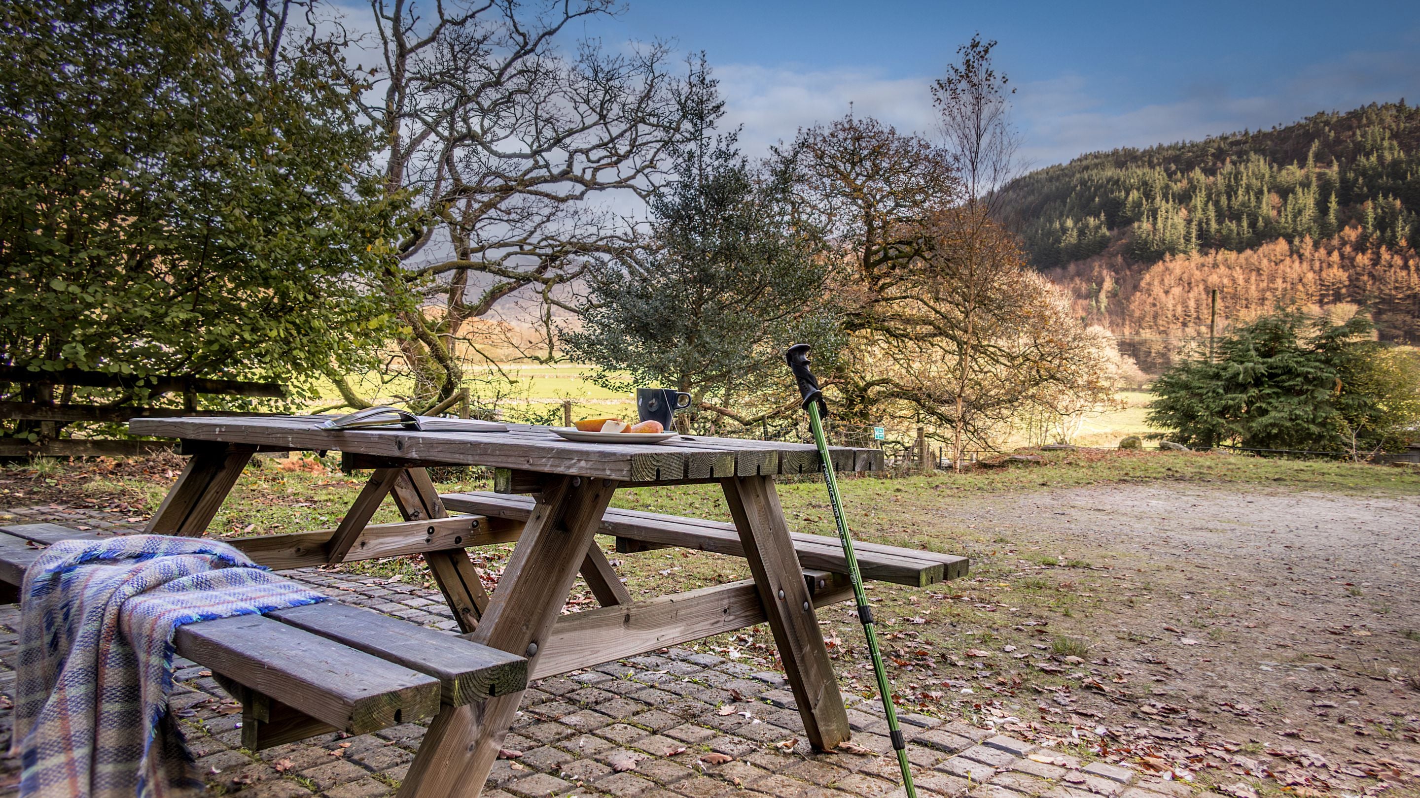 The picnic bench on the patio outside the front of Watkin Bunkhouse, with hills and woodland in the distance, Gwynedd