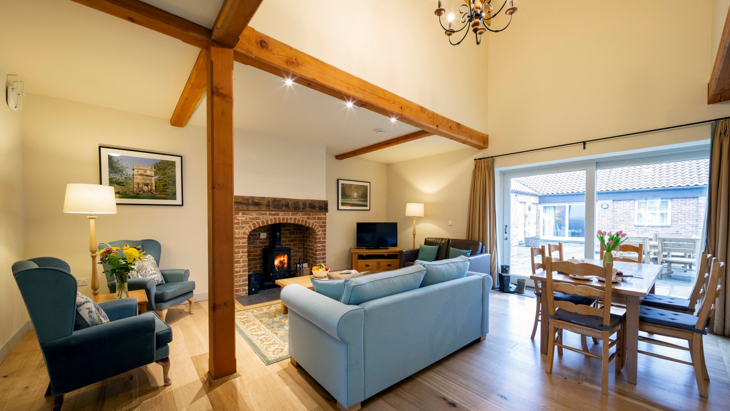 The open-plan living space has double-height ceiling above the dining table and patio doors to the courtyard, at Curlew, Yorkshire