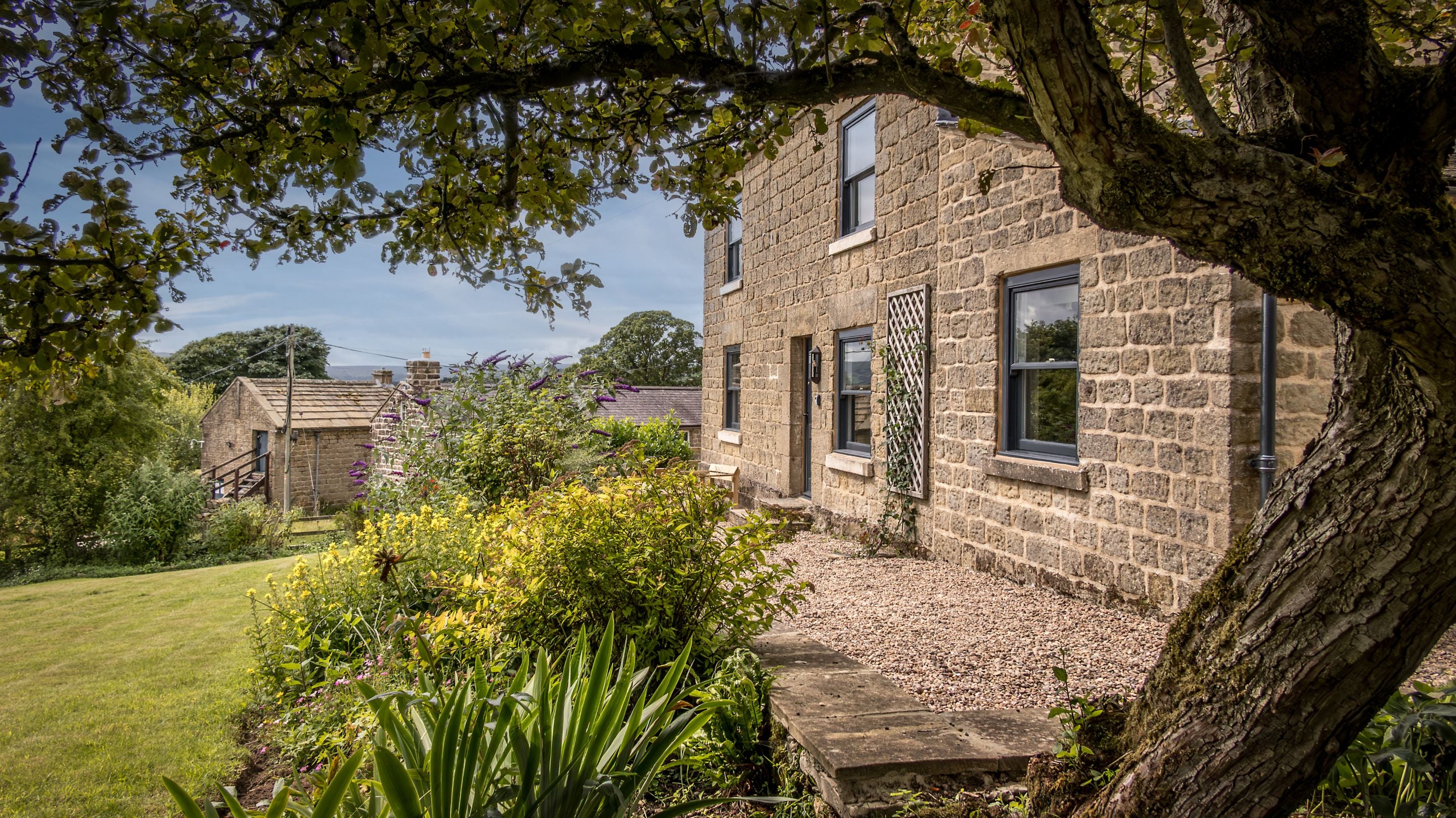 The garden with lawn, flower beds, gravelled patio and tree at Druid's Cave Farmhouse, North Yorkshire