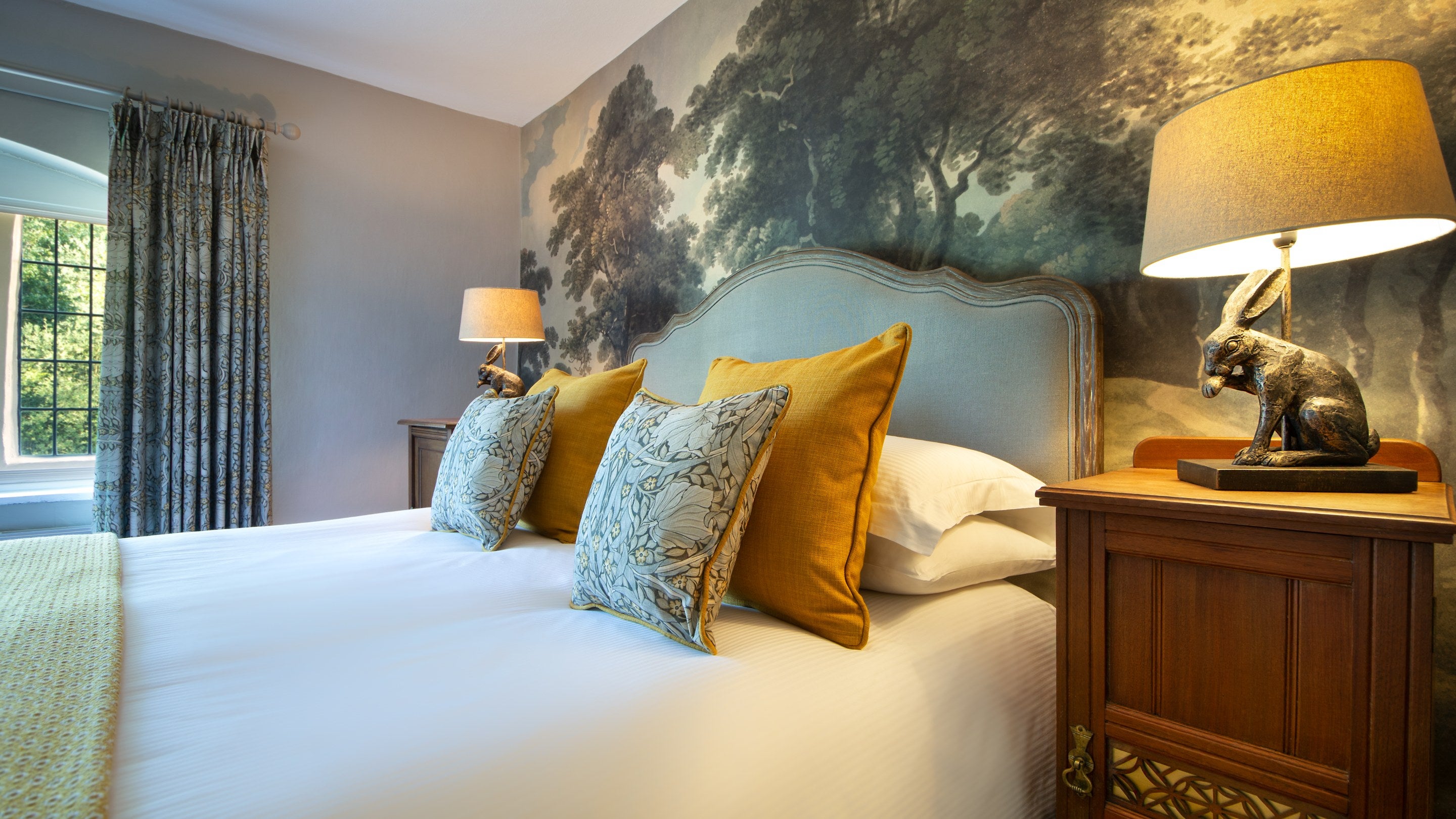 One of the king-size beds on the first floor of Fountains Cottage with mural wallpaper of woodland behind the bed, Yorkshire