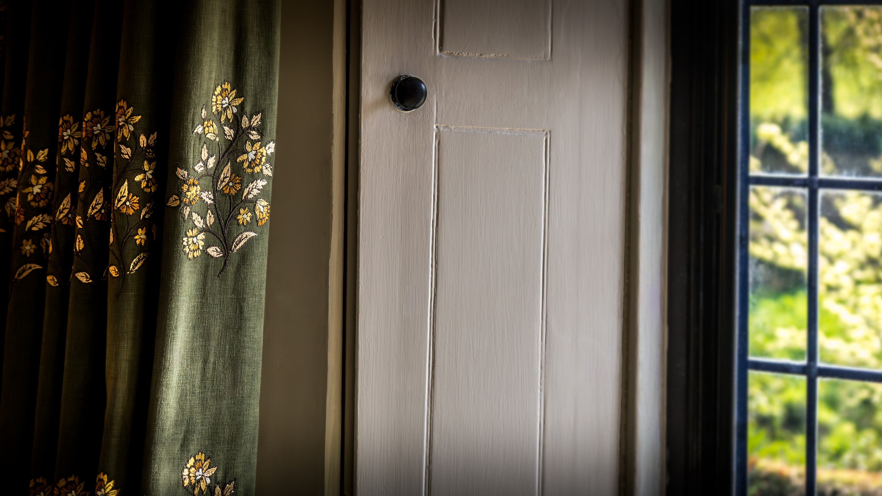 A lattice window in the sitting room at Fountains Cottage, with white shutters and dark green curtains, Yorkshire