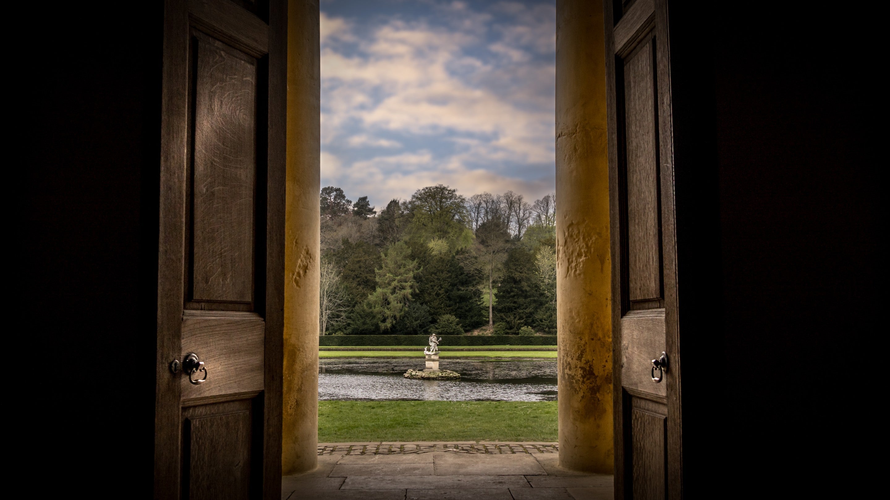 Looking out from one of the temples at Studley Royal Water Garden to an ornamental lake with a stature in the middle, Yorkshire