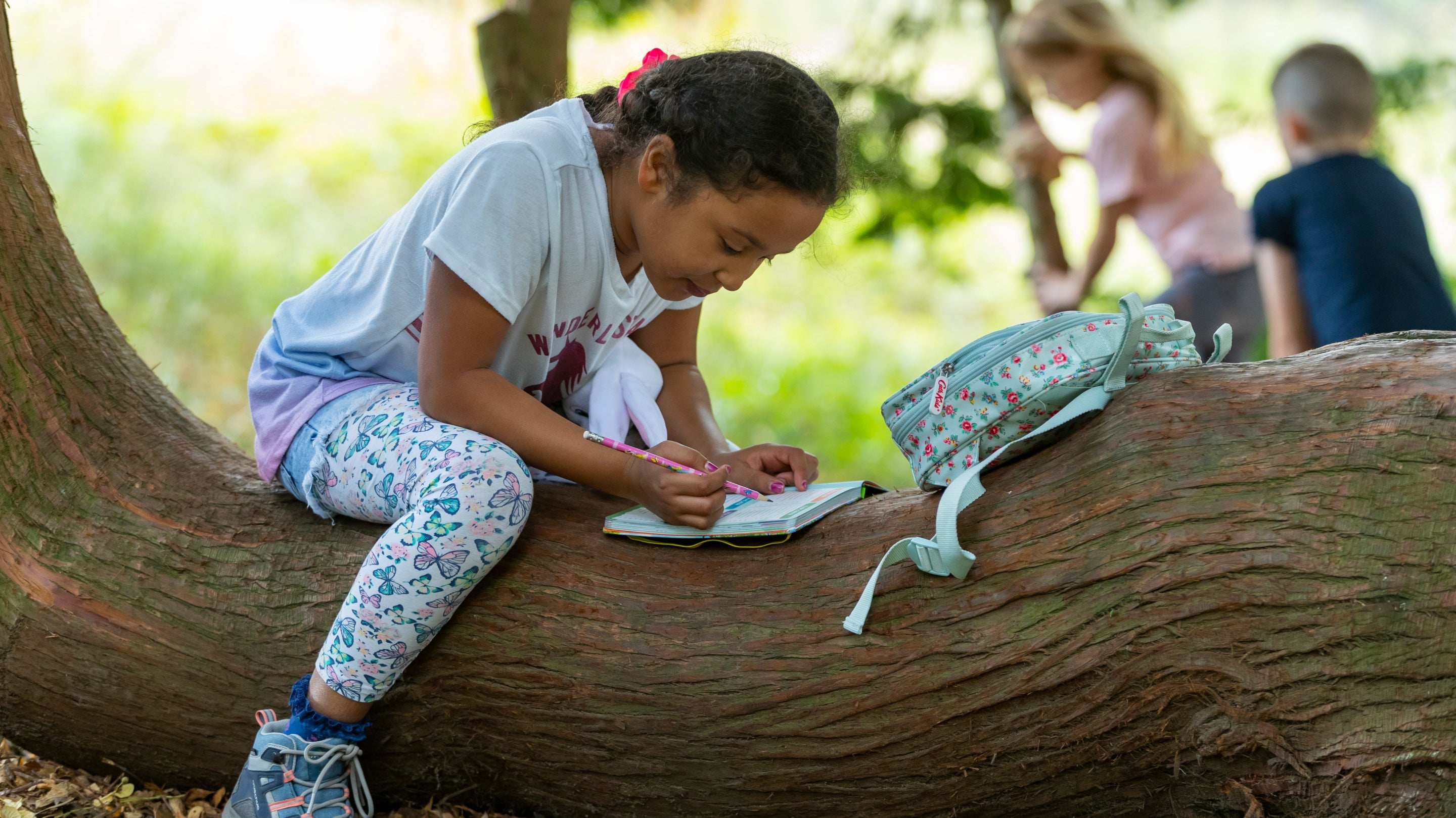 A girl sits on a tree trunk writing in her notebook at Lyme Park, Cheshire