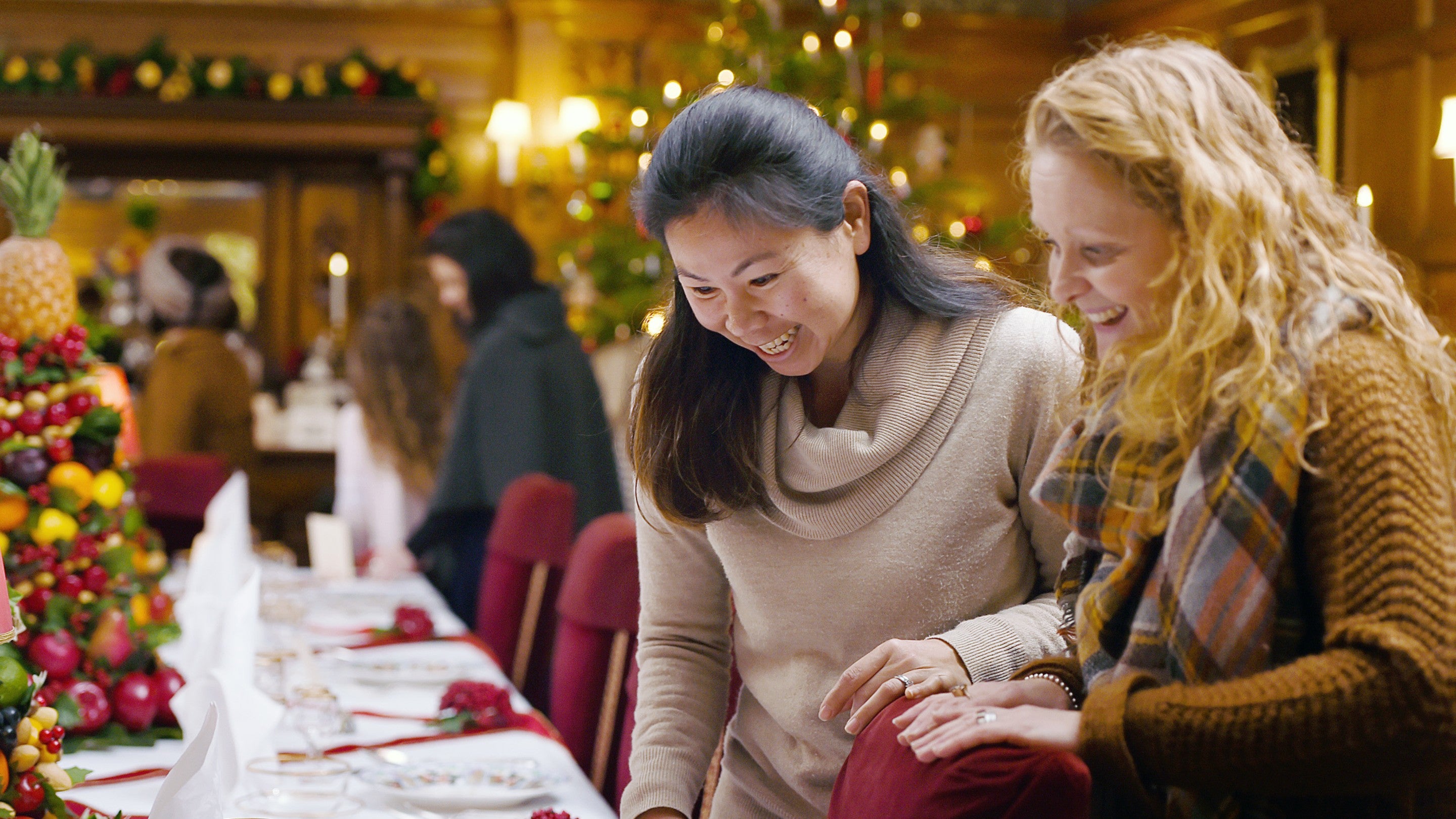 Two women admiring the settings on the table in a hall decorated for Christmas at Lanhydrock, Cornwall