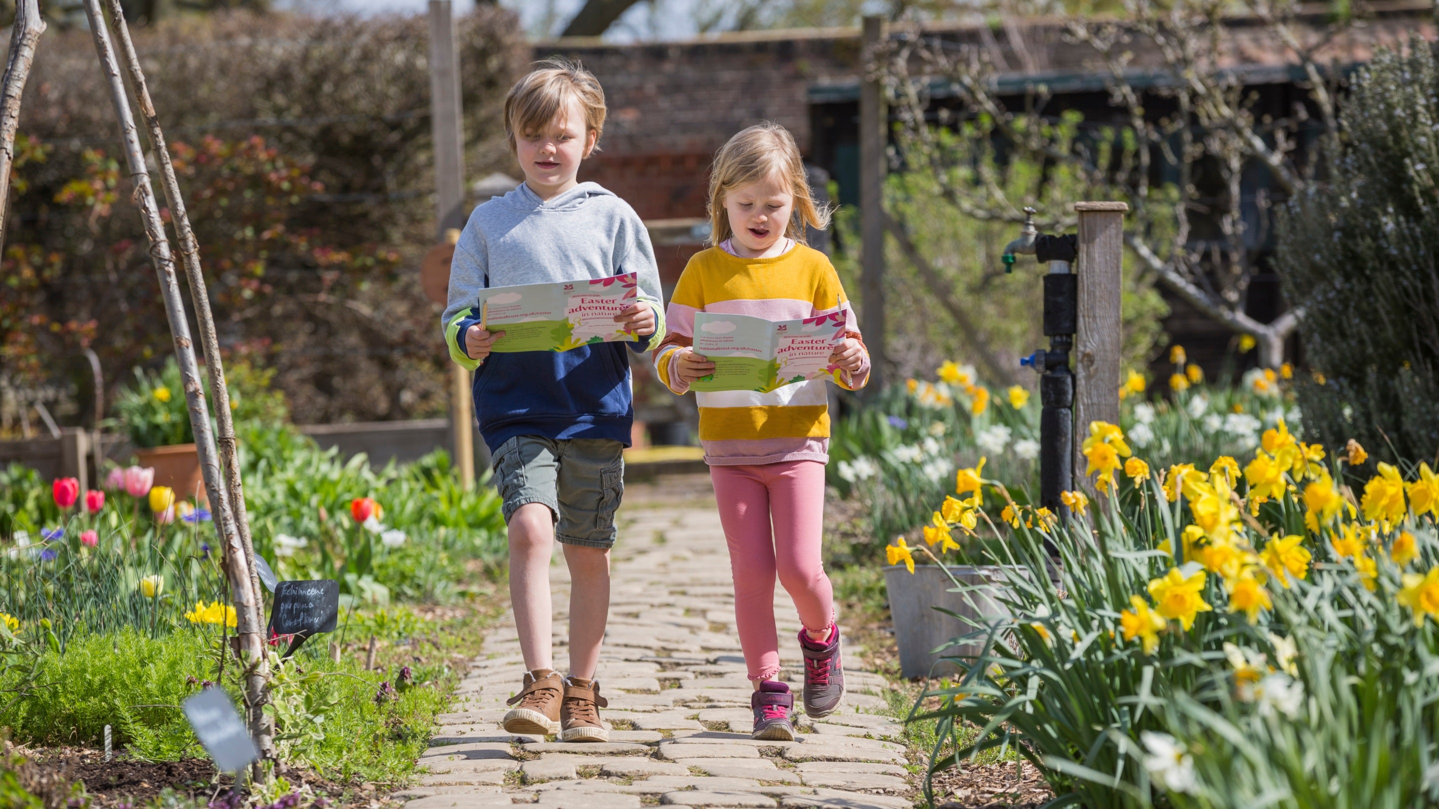 Children walking down a garden path flanked by flowers on the Easter trail at Osterley Park and House, West London