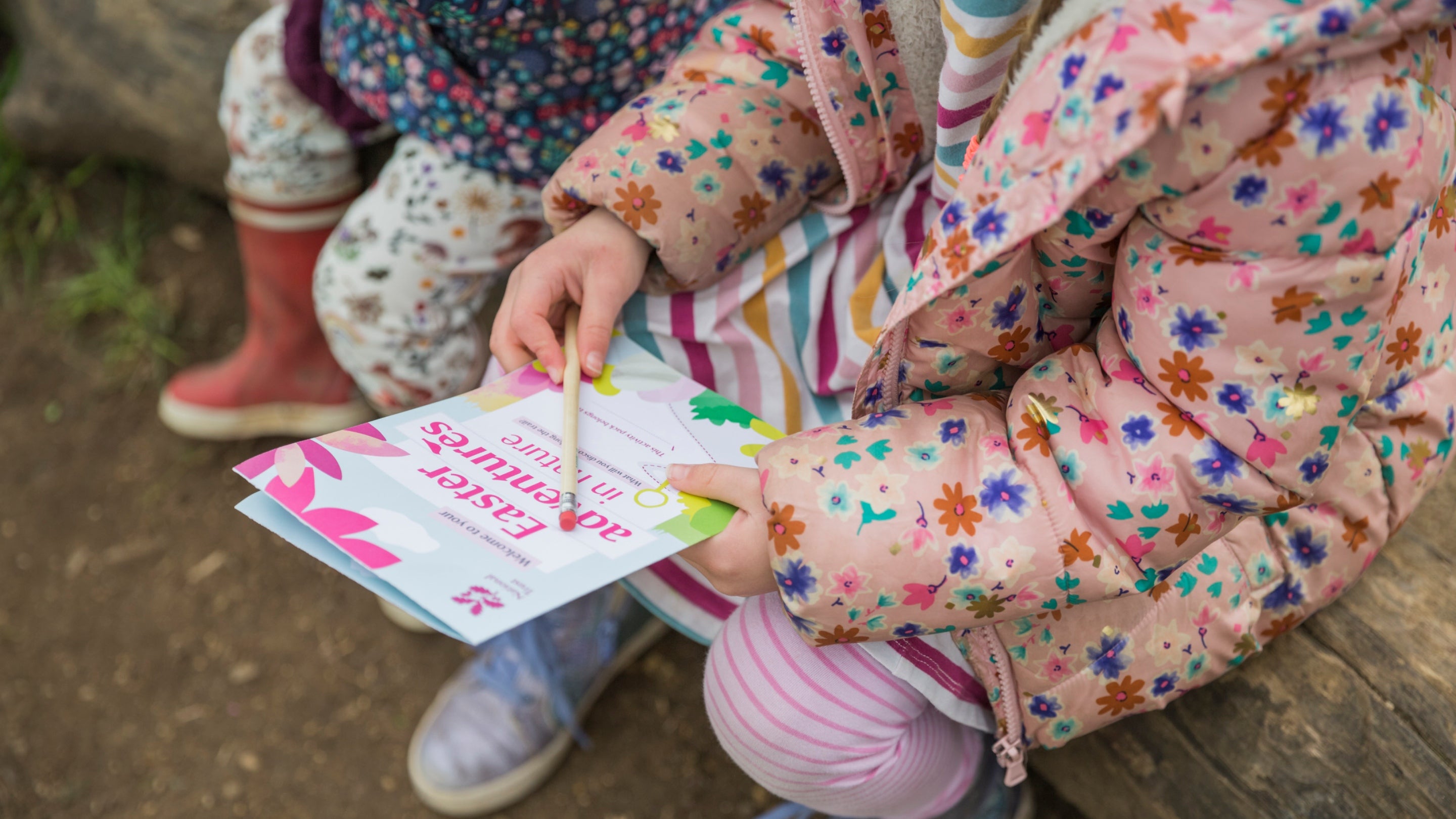 Two children sitting on log looking at Easter trail sheet