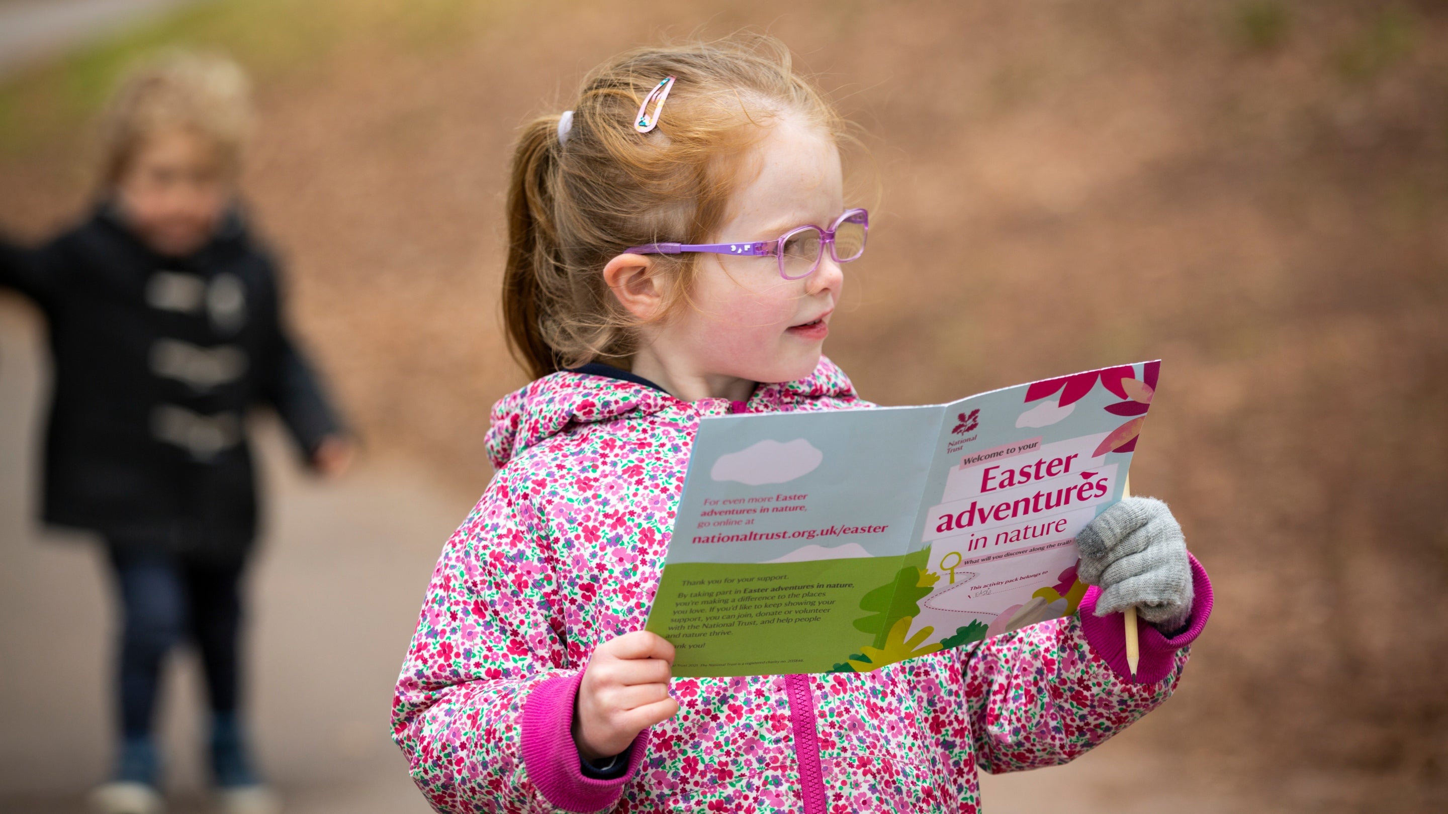 A girl in a pink flowery jacket and glasses holds a leaflet on the Easter trail at Tyntesfield, Somerset
