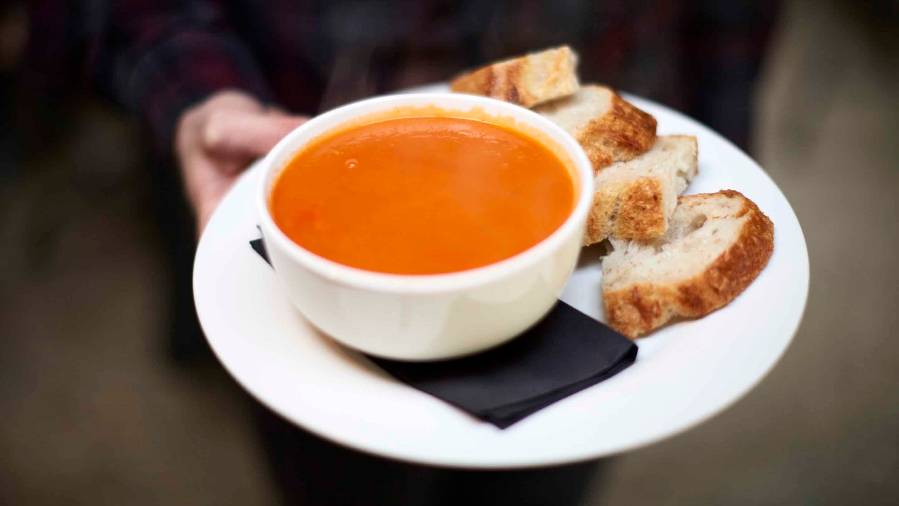 A close up of soup and bread being served by a catering assistant