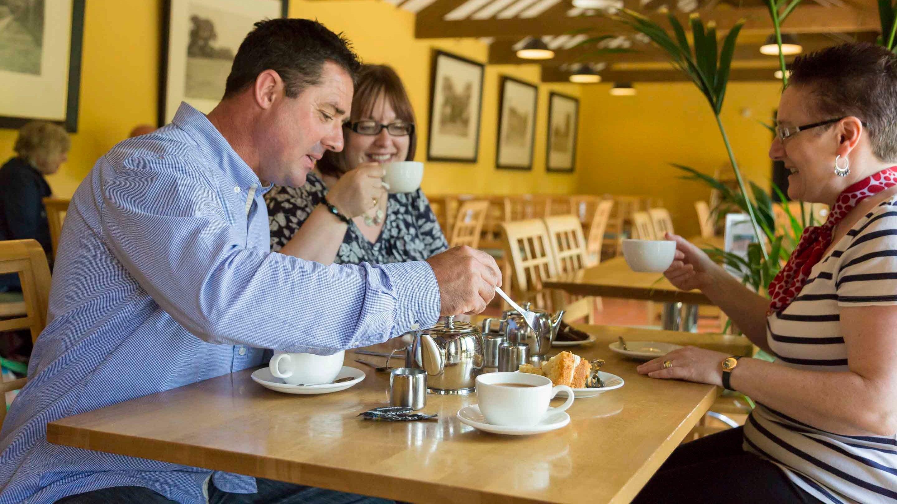 Three visitors sat at a café table with tea and cake