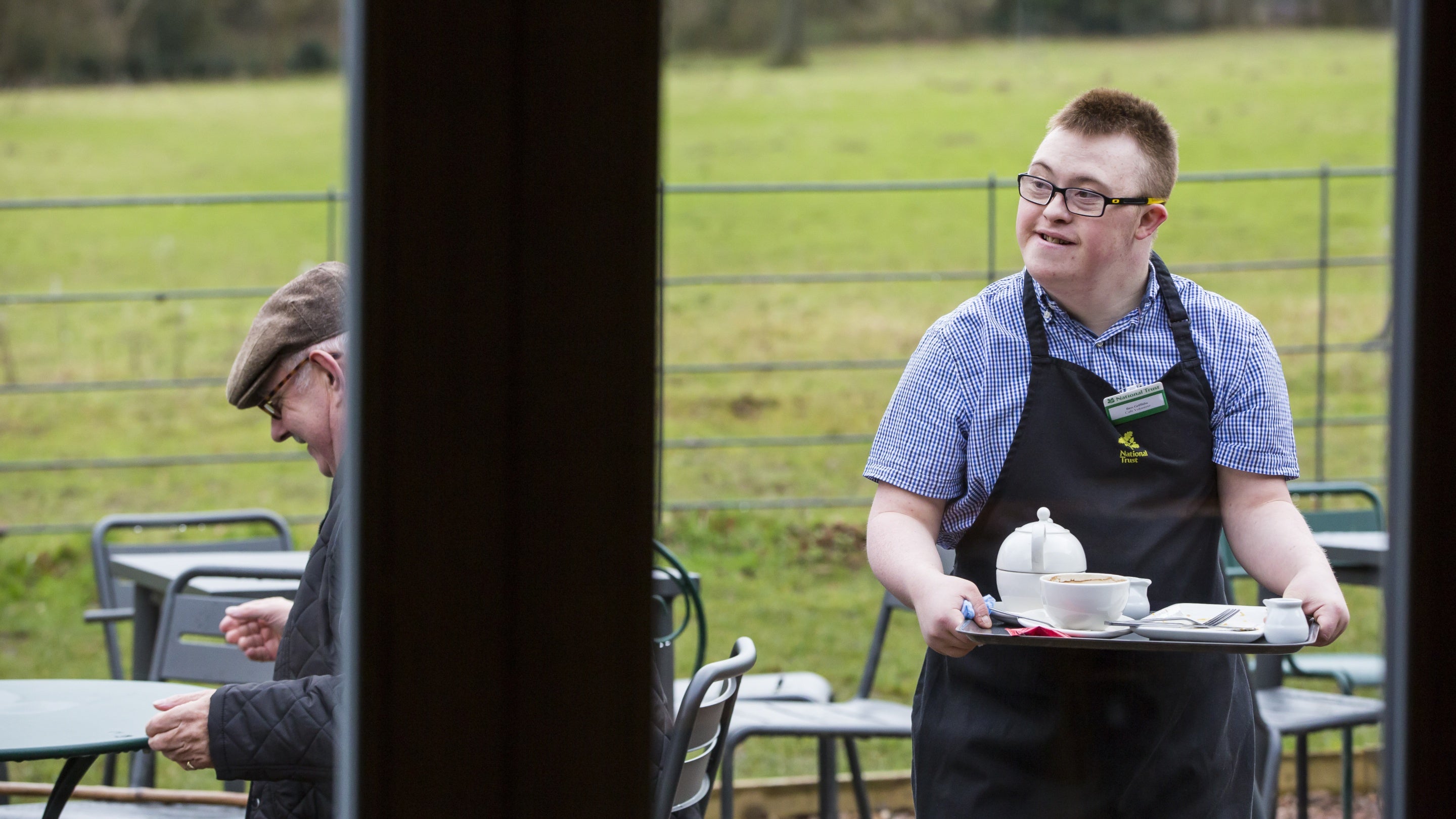 Volunteer catering assistant carries a tray of hot drinks outside the Kitchen Garden Cafe at Packwood House, Warwickshire