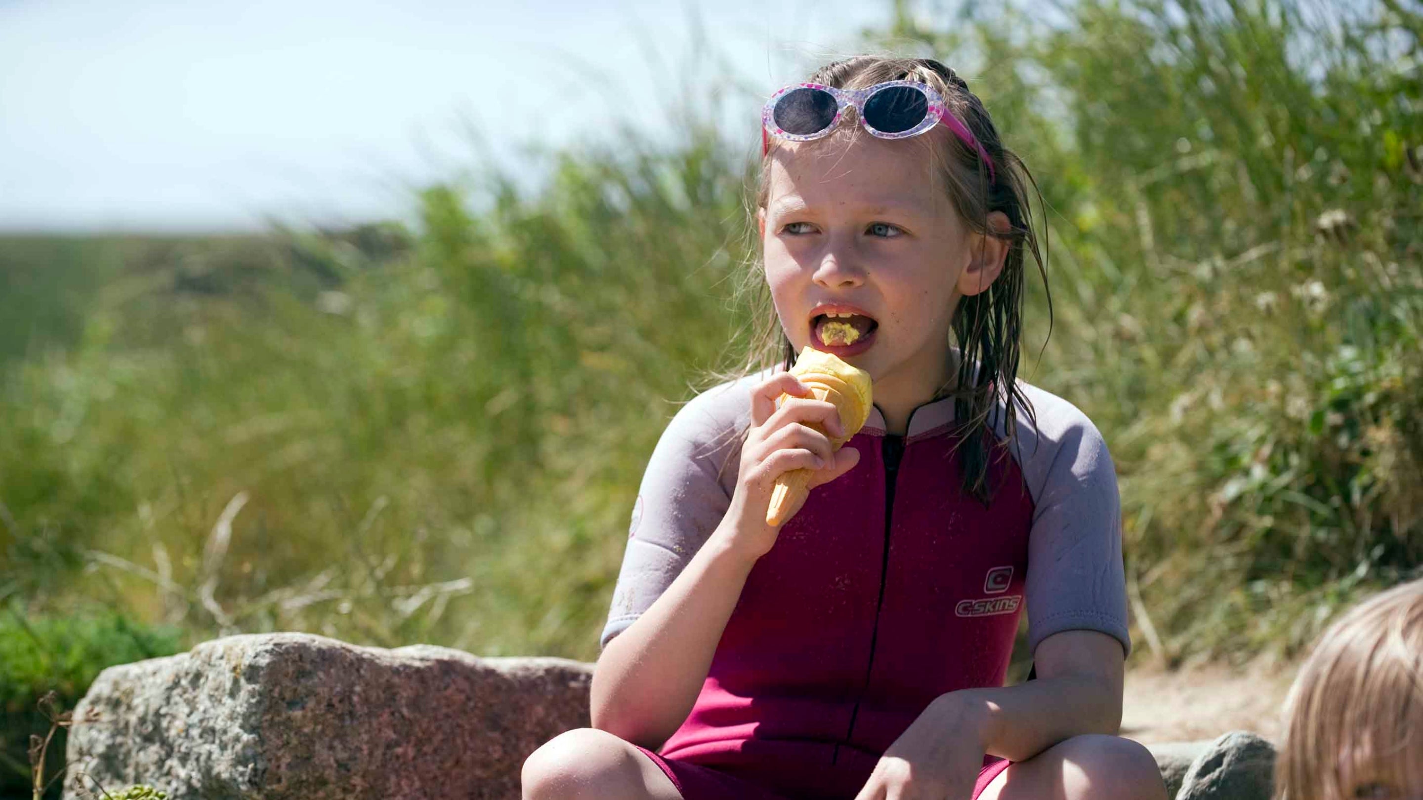 A child eating ice cream while wearing a surf suit