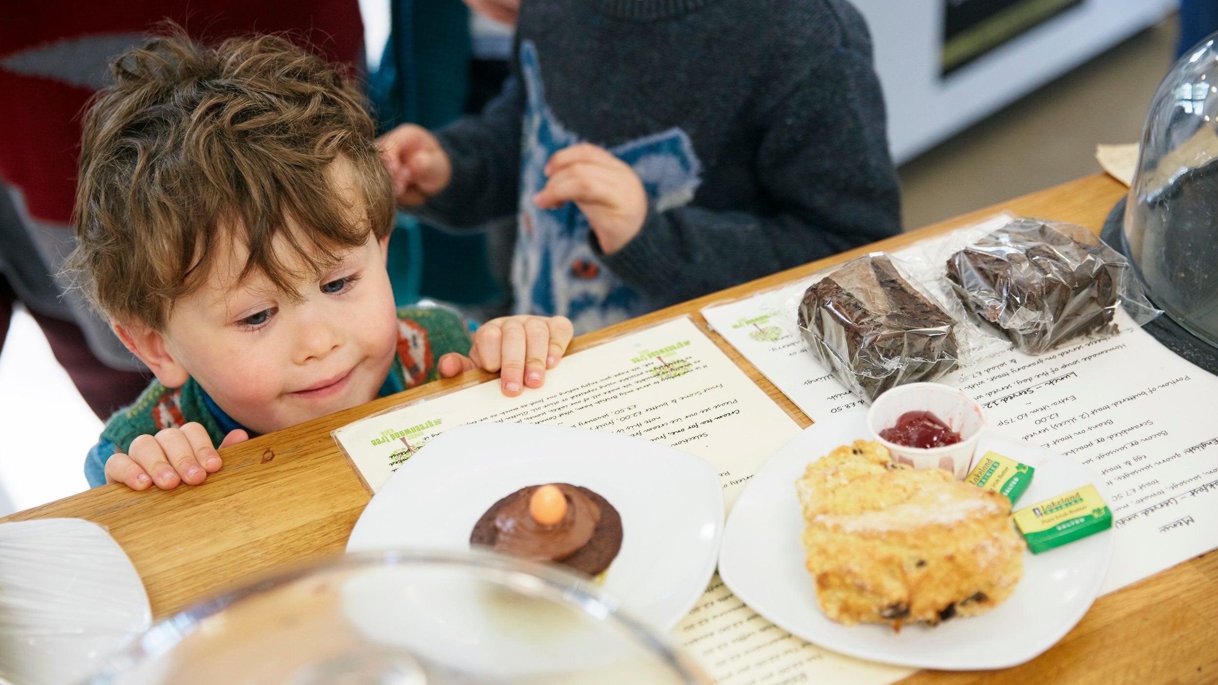 A young child peaking at cookies and scones on a table