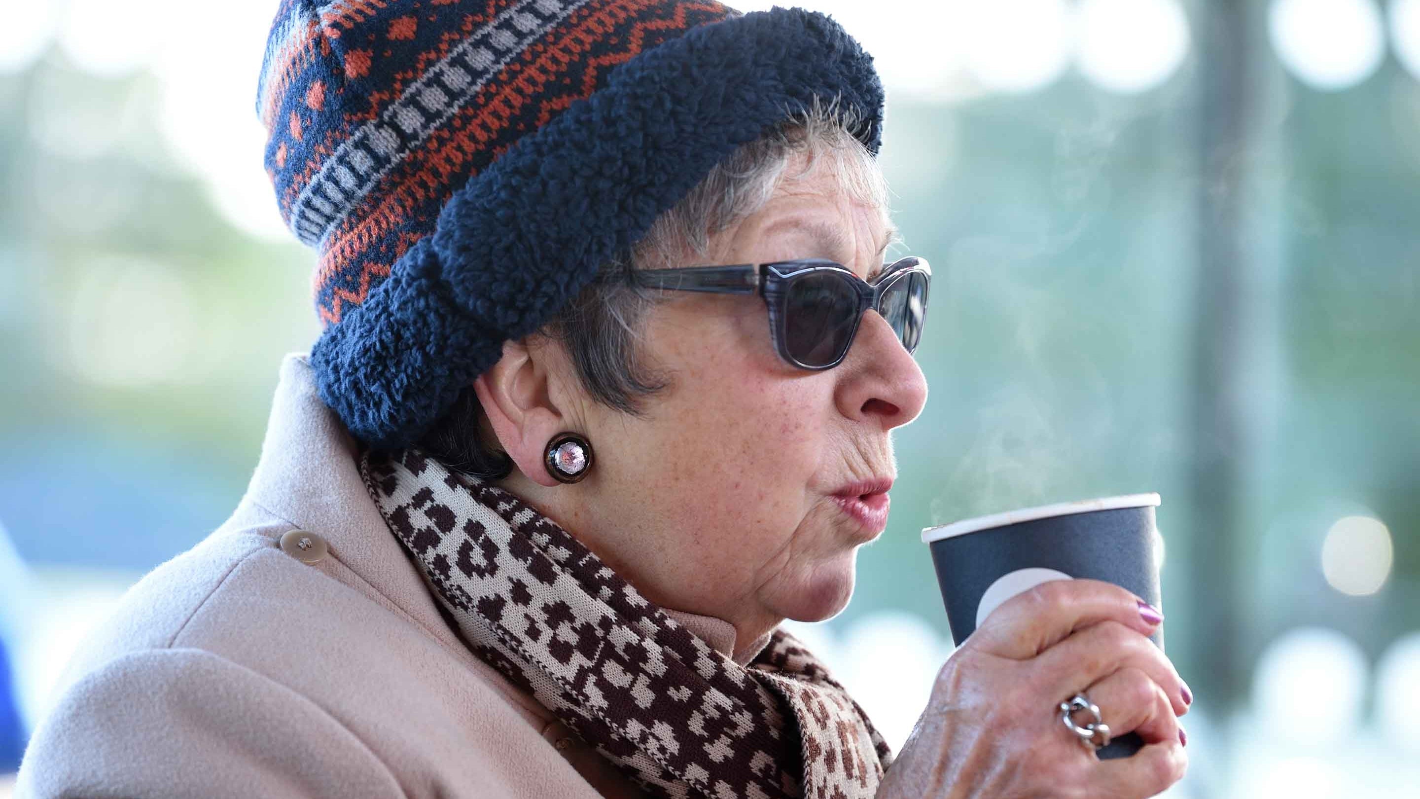 A woman in a hat and scarf drinking from a takeaway cup