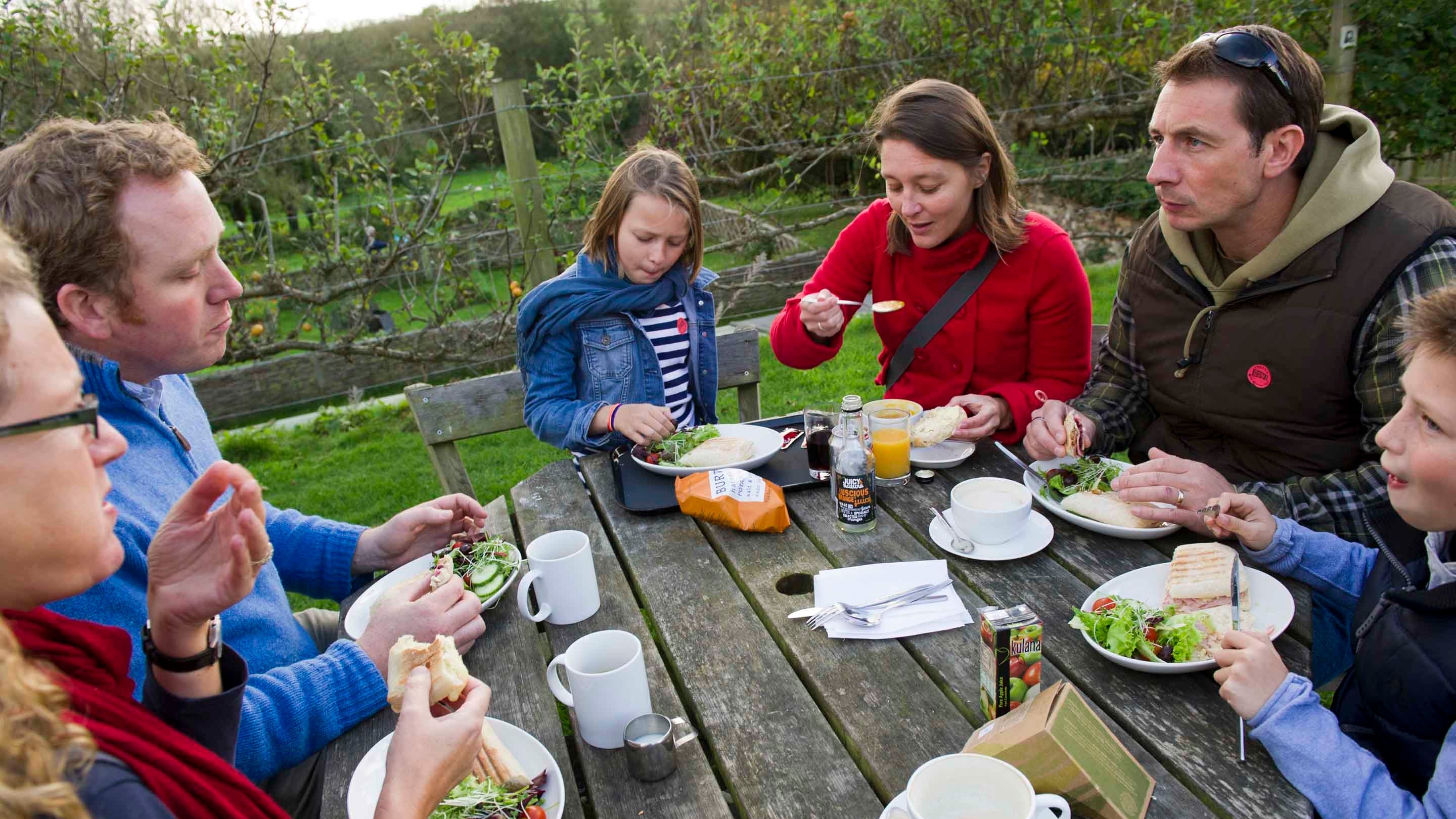 Visitors sat around a bench having lunch outside at Trerice, Cornwall