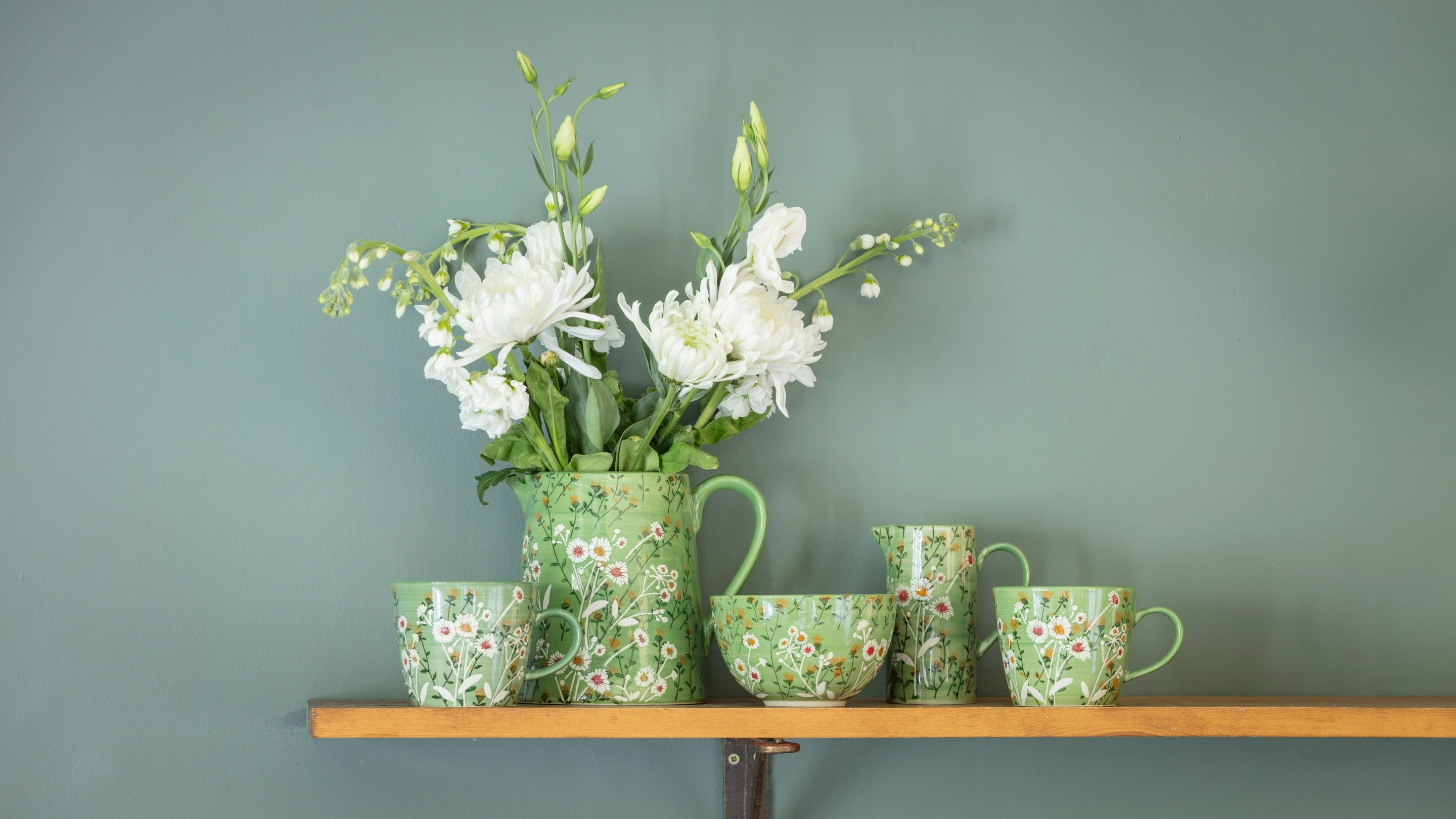 A selection of green ceramic mugs, jugs and a bowl all decorated with a white daisy pattern from the 2025 autumn/winter collection