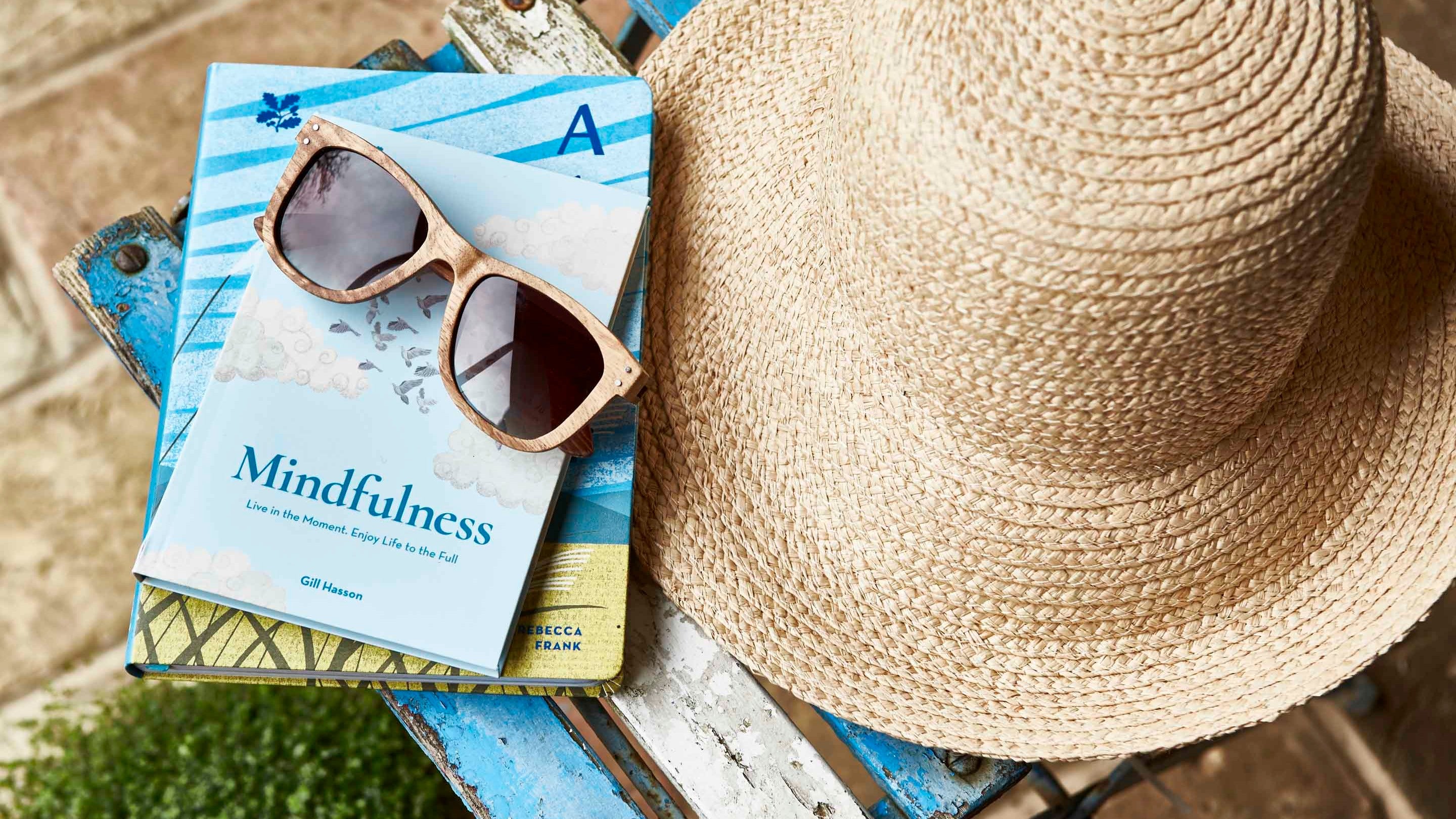 An overhead shot of a sunhat, sunglasses and a book balanced on a chair