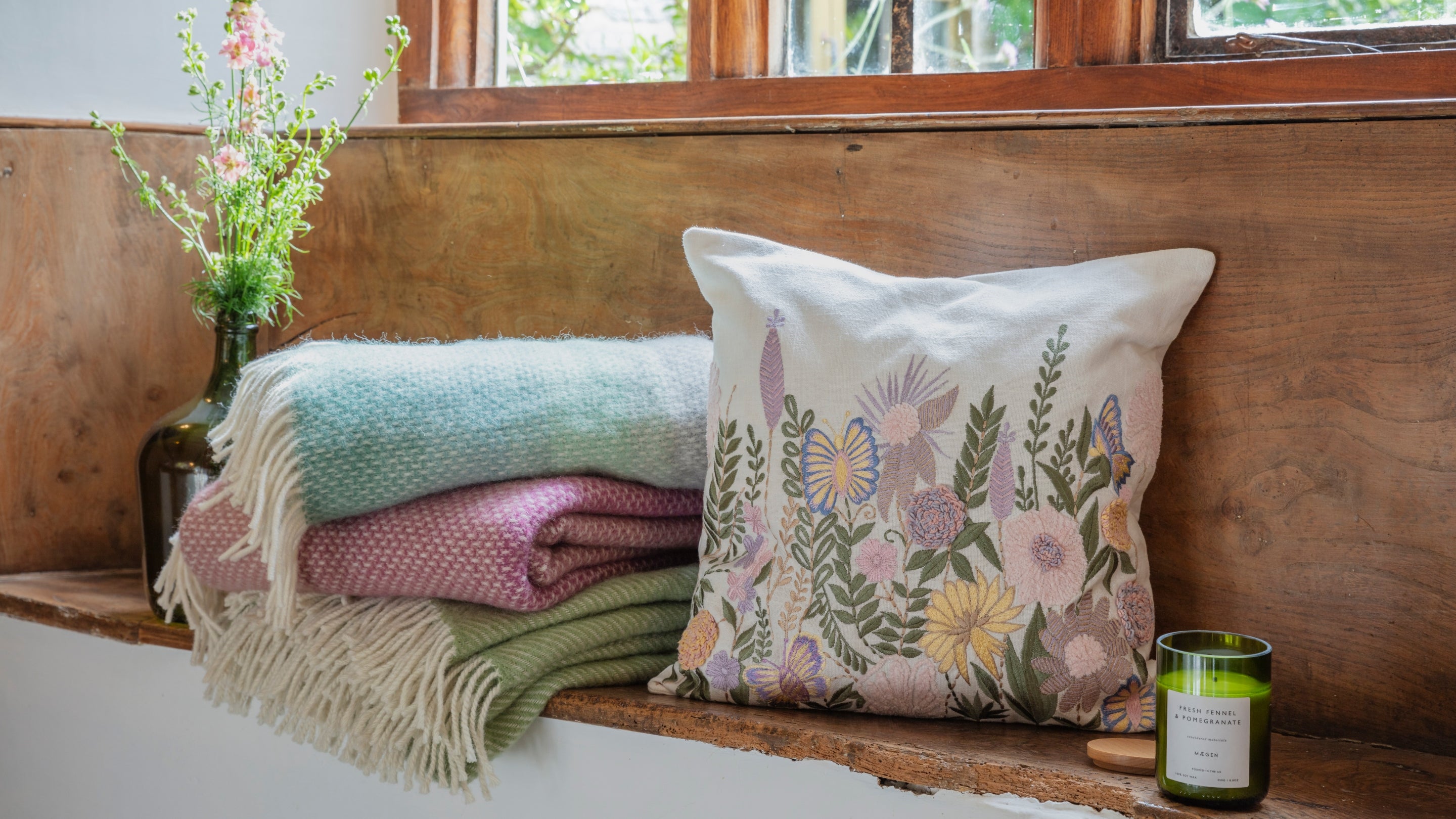 A cushion with a floral decoration and colourful pastel throws