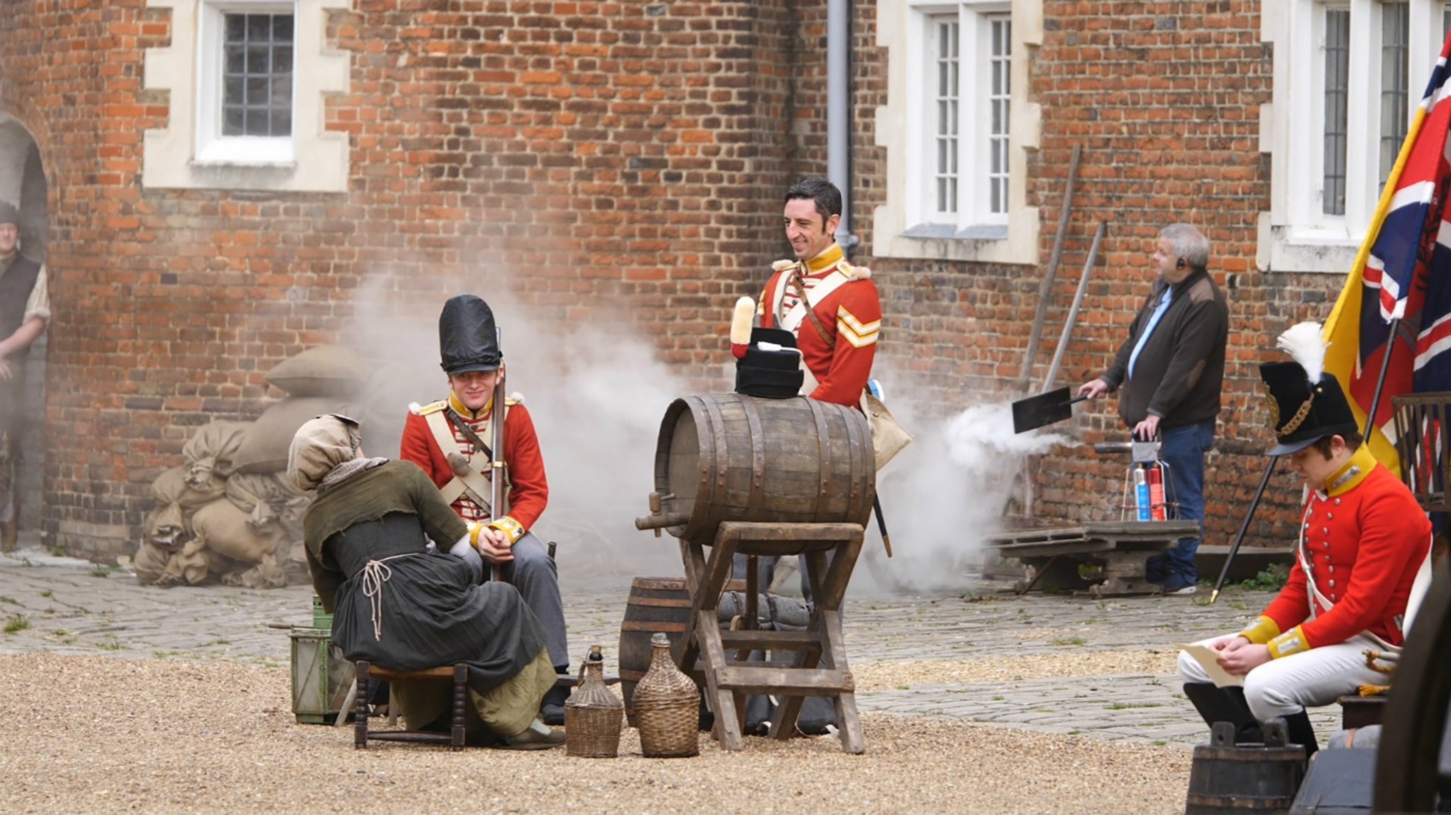 Actors in soldiers' uniforms in a scene in Osterley's stableyard, while a technician creates smoke effects