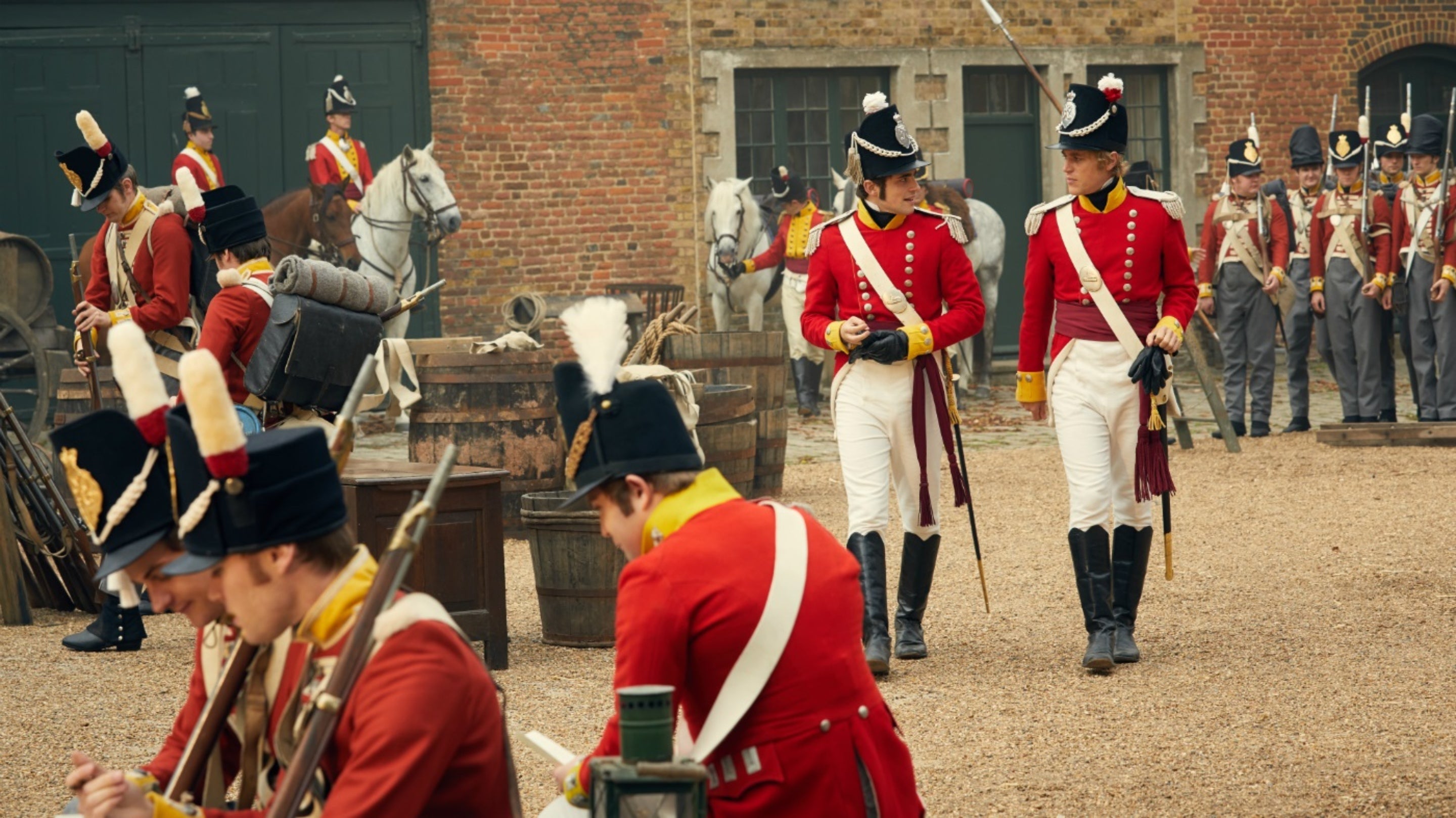 Actors in red soldiers' uniforms walk through the stableyard at Osterley