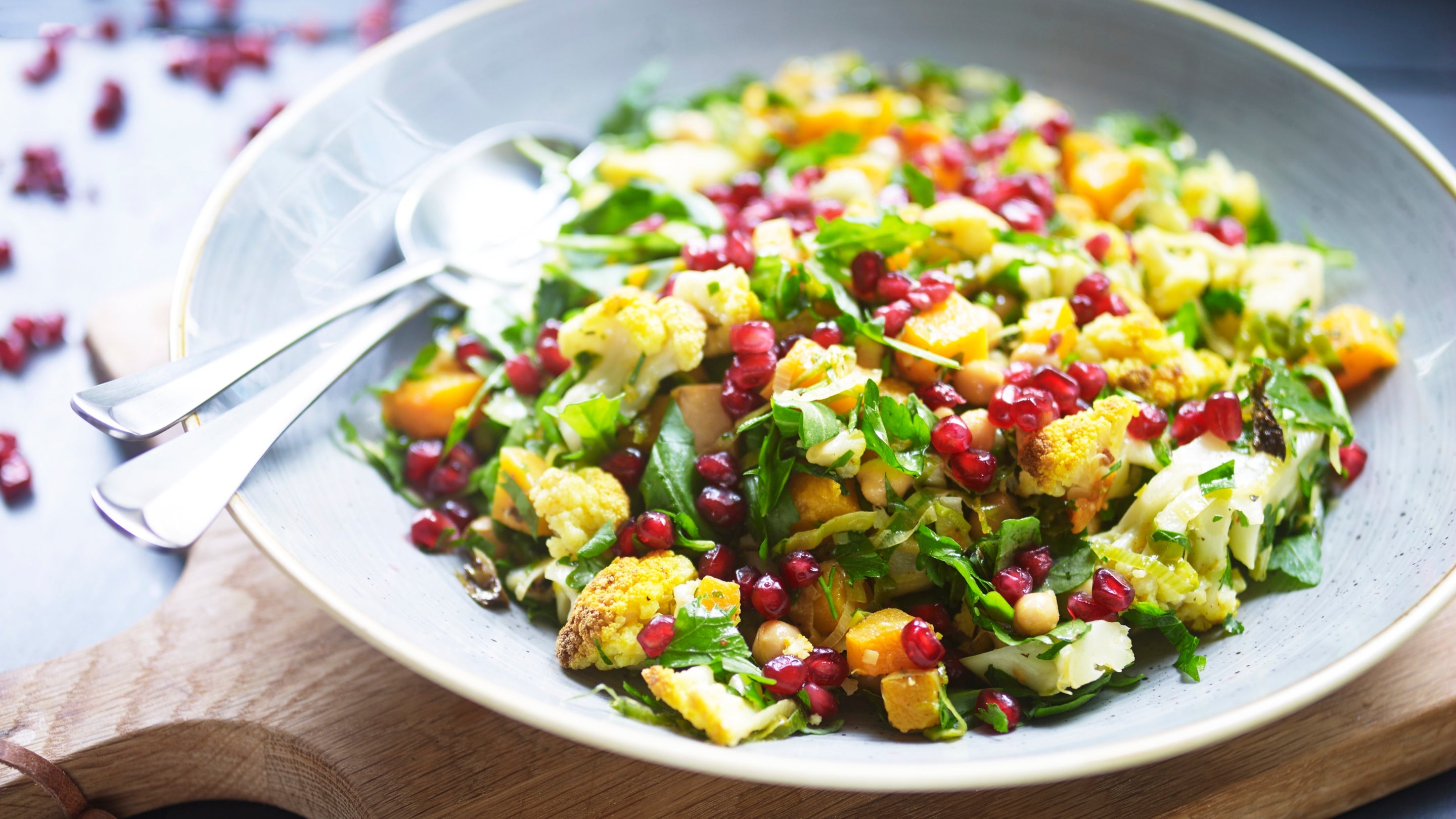 Moroccan-style roasted cauliflower salad in a bowl with cutlery, placed on a wooden board