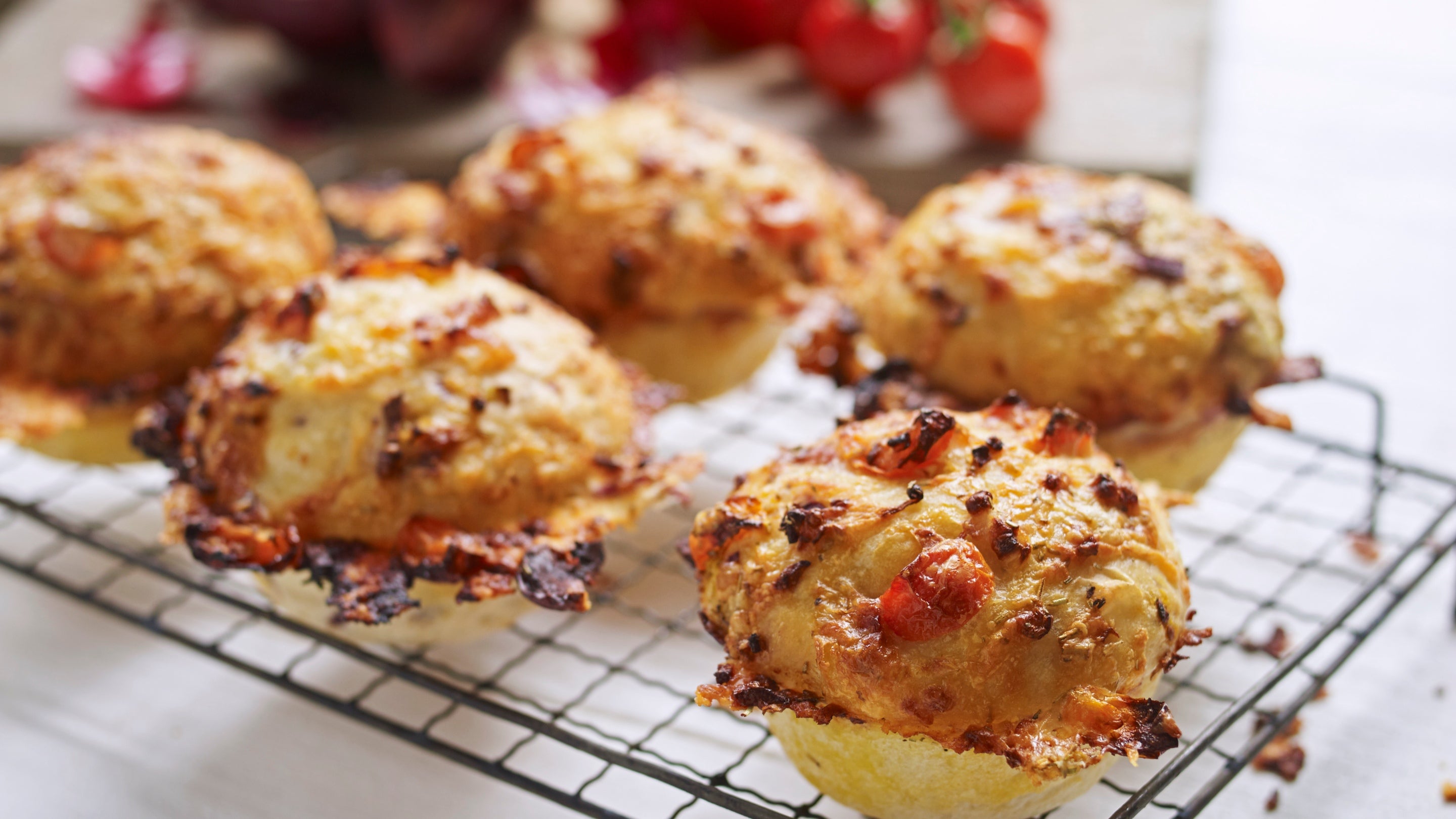 Cheese and tomato muffins on a rack with tomatoes behind them