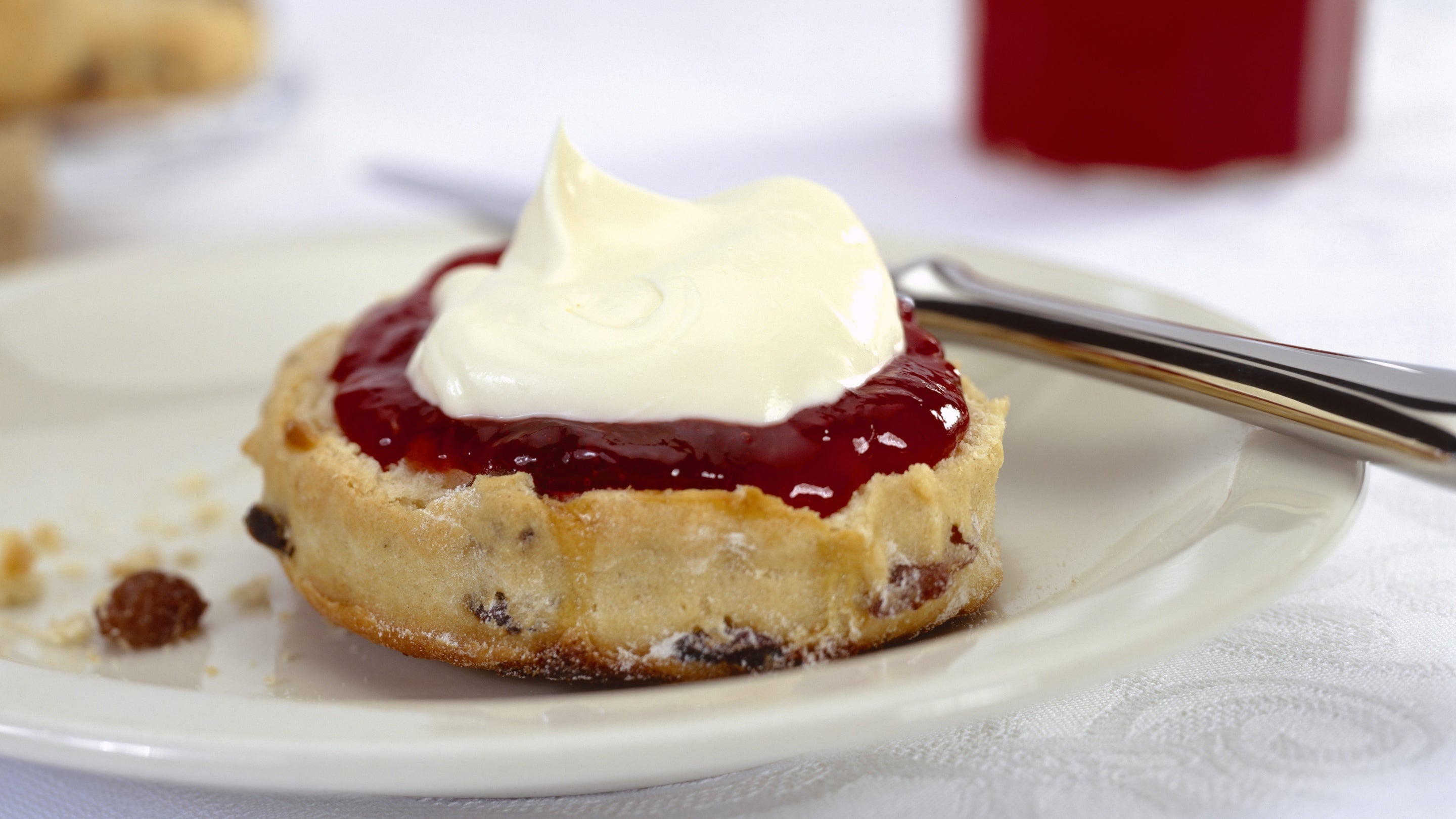 A close up view of a scone served on a plate with a generous helping of jam and cream