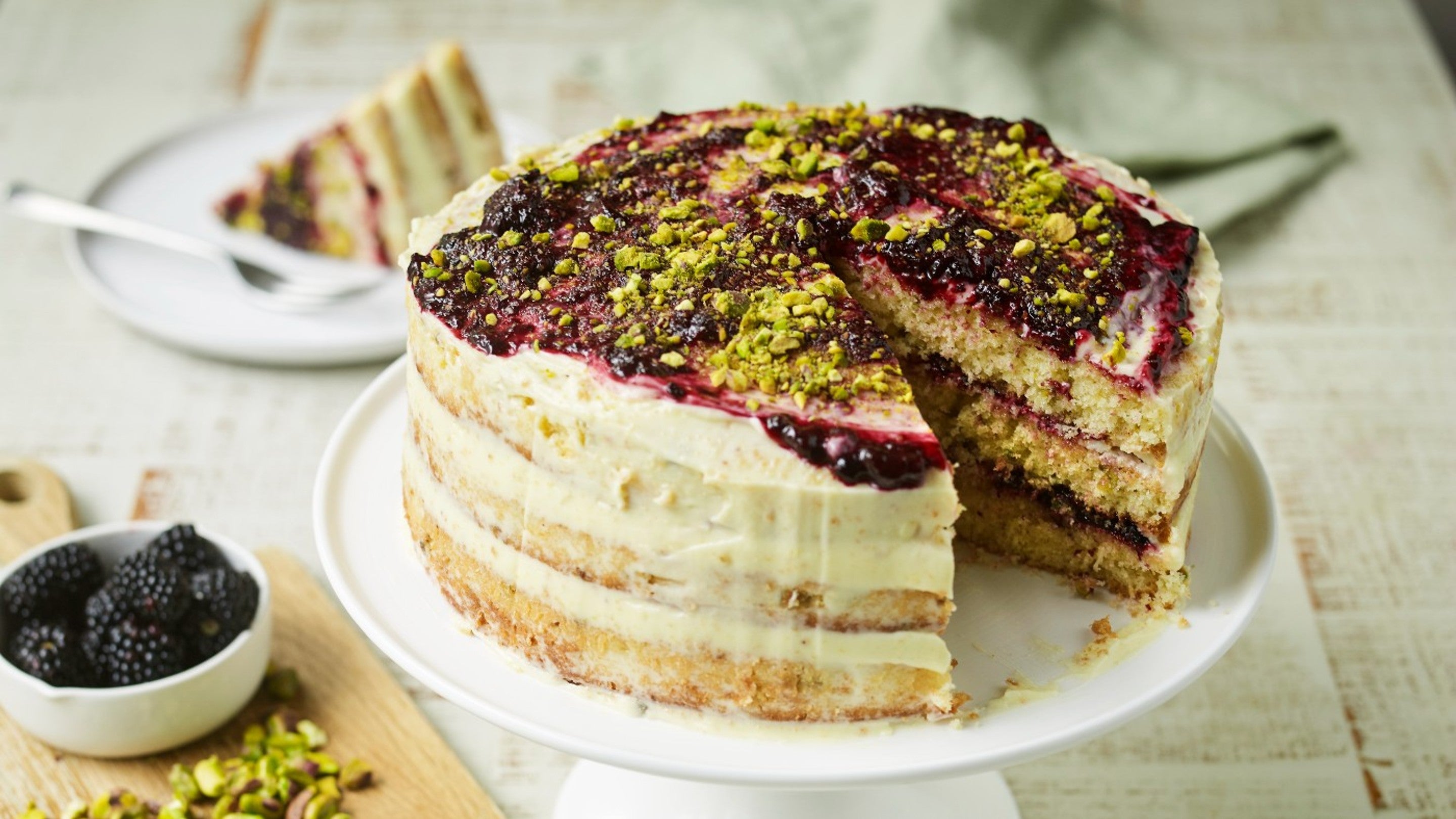 Blackberry and pistachio cake with a slice removed and on a small plate