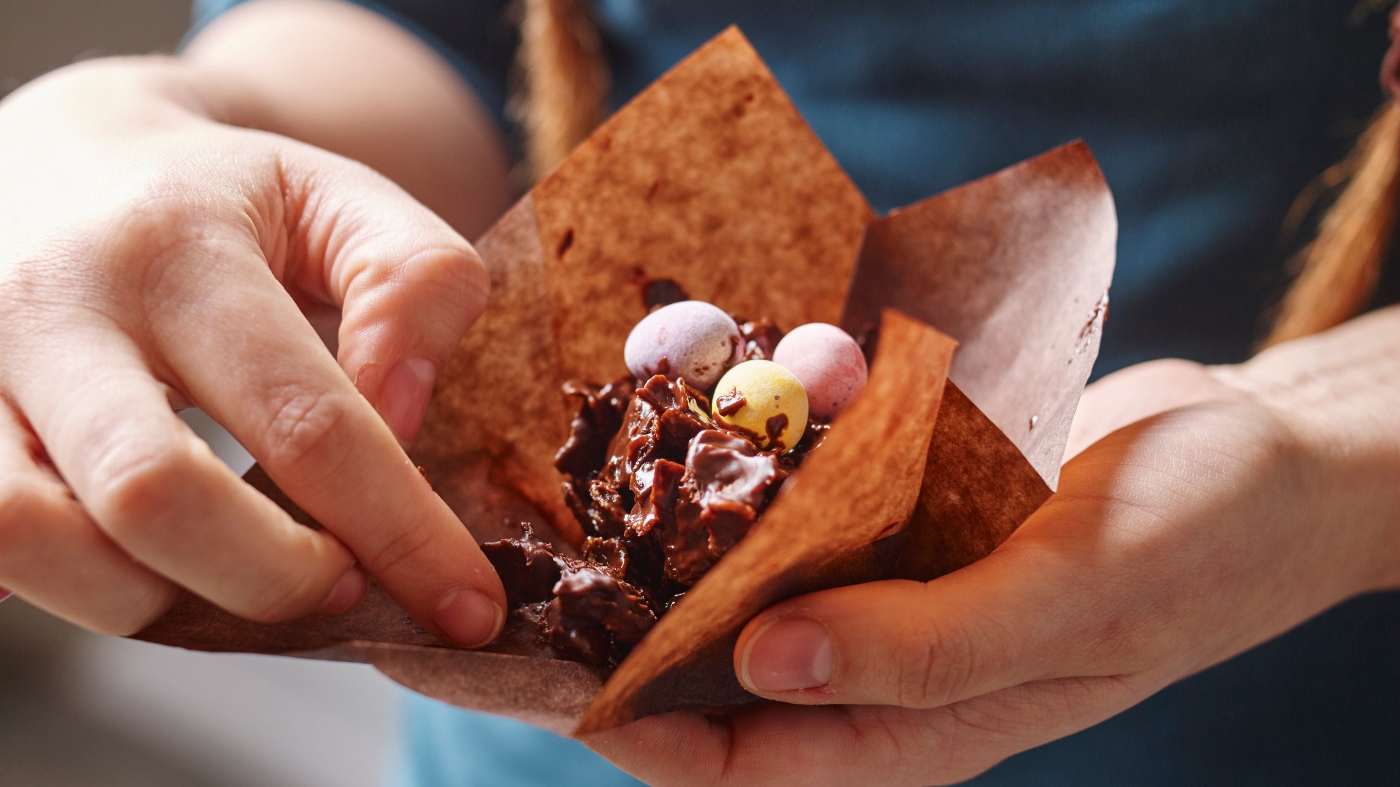 A person unwraps the paper muffin case of a chocolate nest