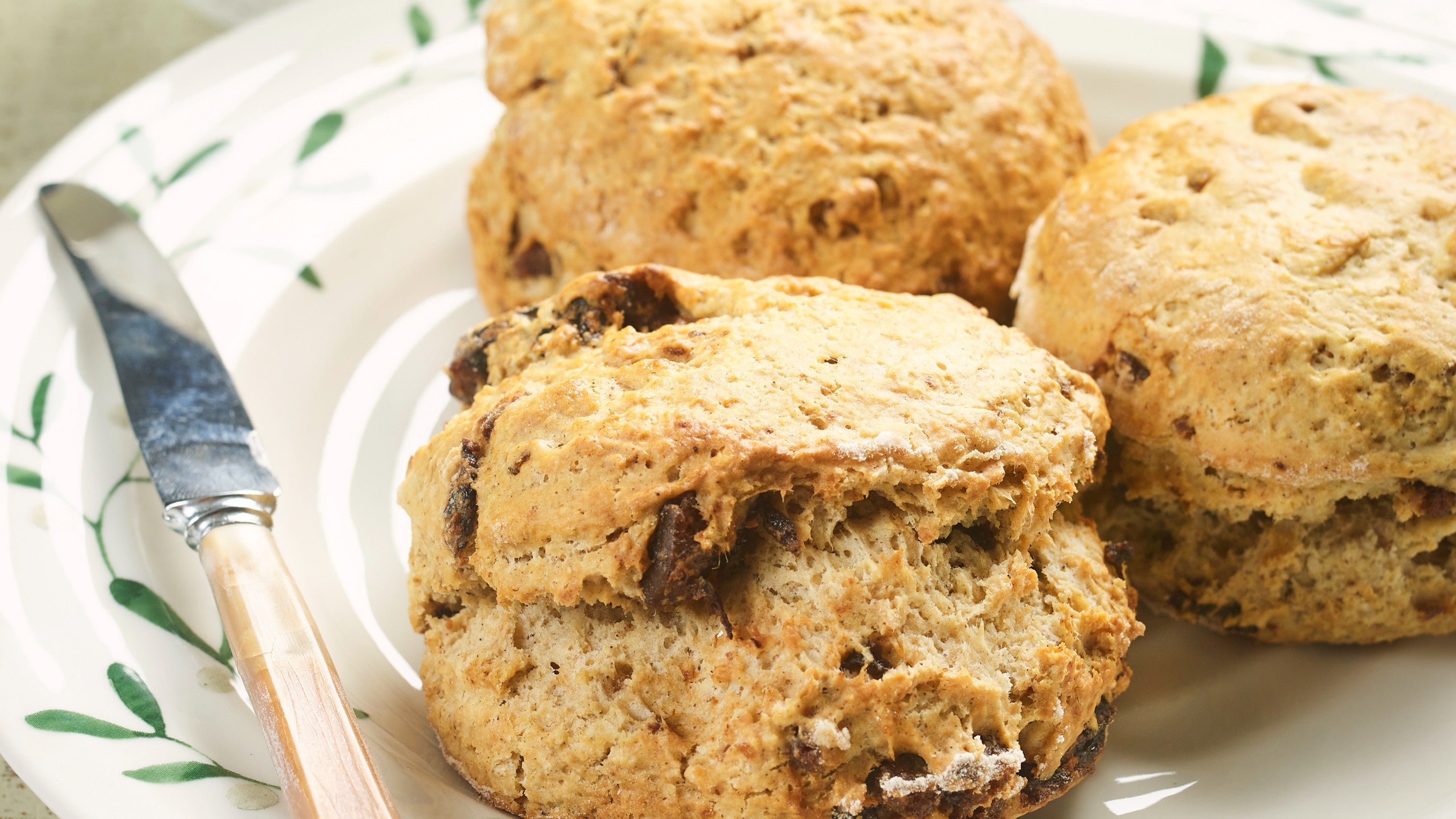 Three baked Christmas pudding scones on a white plate next to a knife