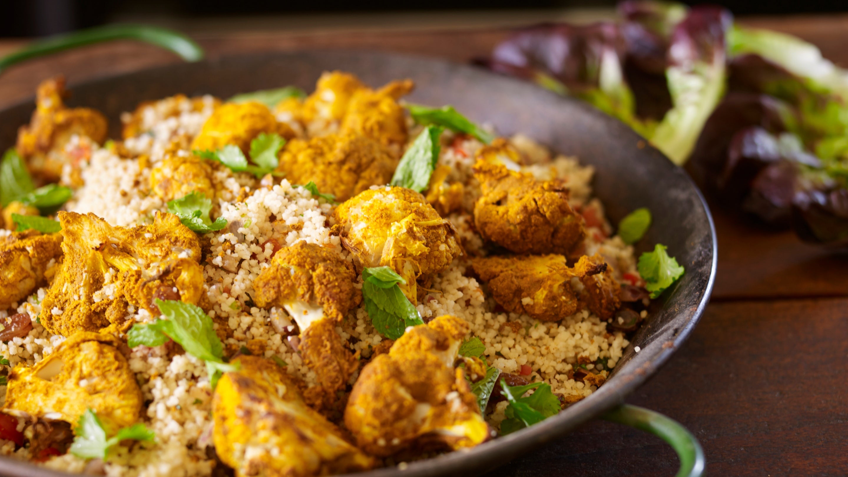 Coronation cauliflower and couscous salad, with golden spiced cauliflower chunks on couscous, scattered with mint leaves