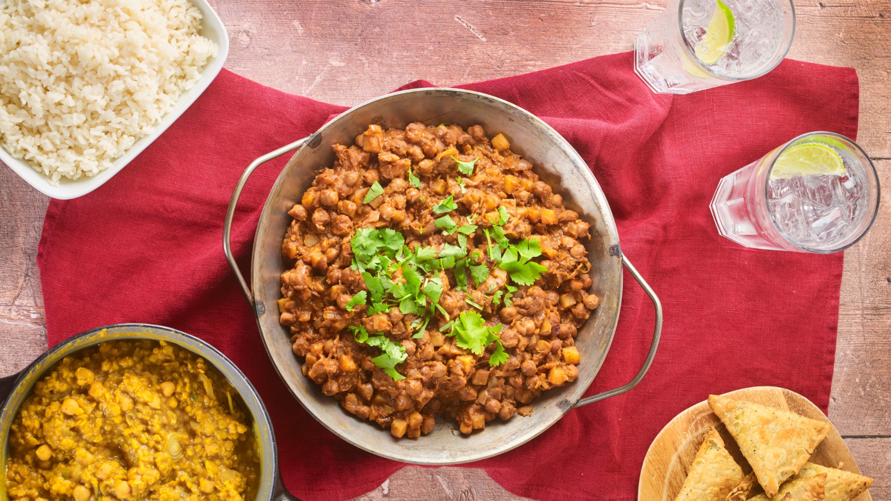 Kedleston chickpea curry in a cooking pot on the table, ready to be served alongside chickpea dhal, rice and samosas